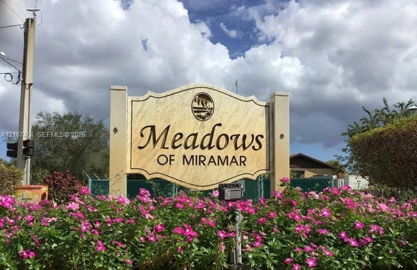9721 W Daffodil Lane, Miramar, FL 33025 Freestanding Meadows of Miramar signage featuring a custom-carved aesthetic, flanked by lush flowering shrubbery and mature landscaping