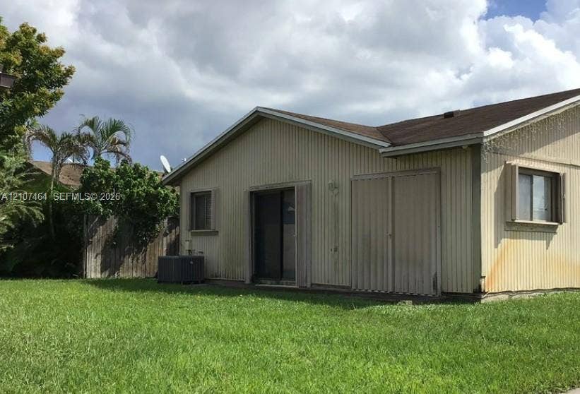 9721 W Daffodil Lane, Miramar, FL 33025 Exterior elevation featuring vertical metal siding, a gabled roofline, sliding glass door, and a grass lawn