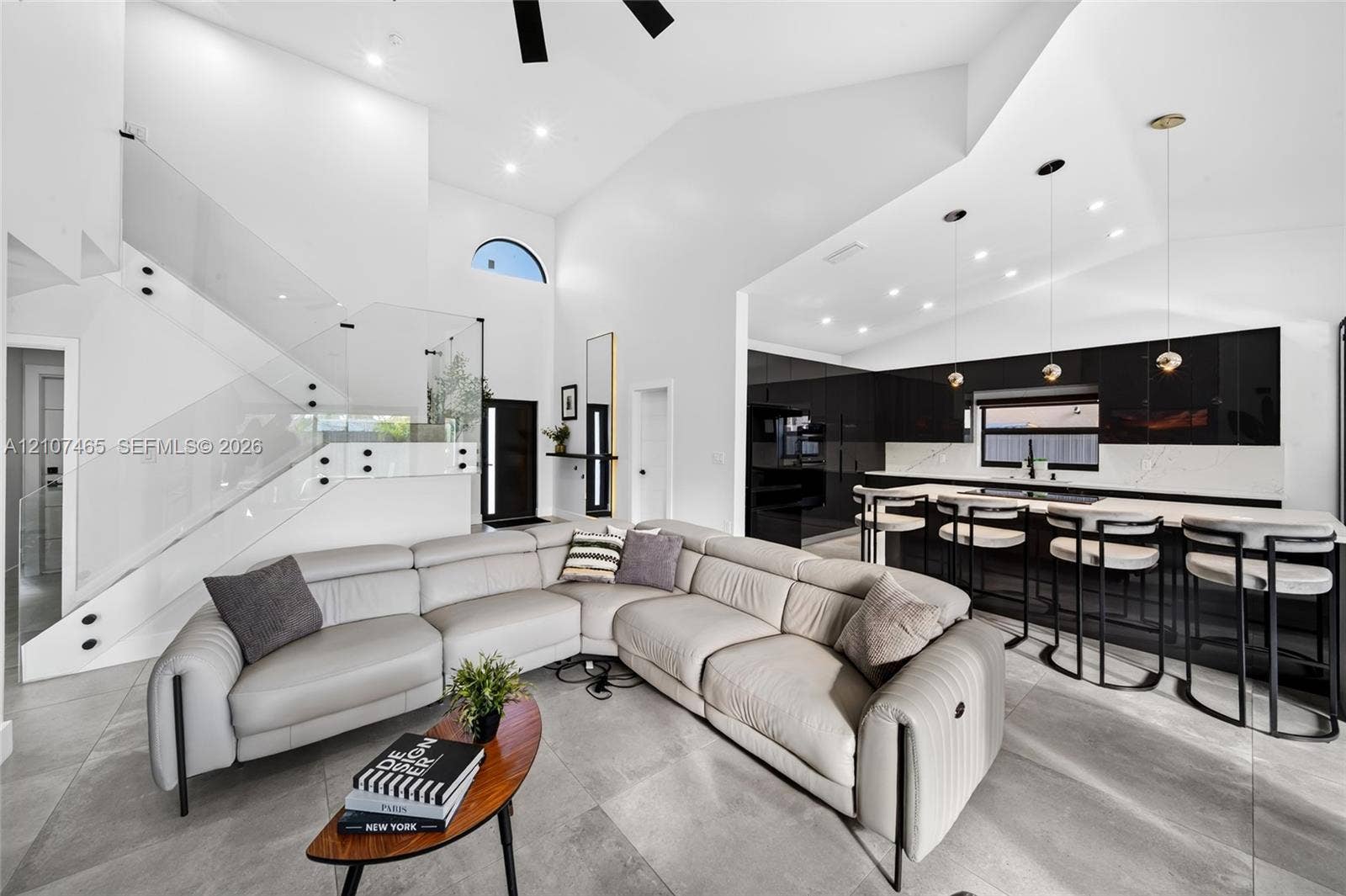 Vaulted ceilings, staircase with glass railings, large-format tile flooring, kitchen featuring black high-gloss cabinetry, and waterfall-edge island