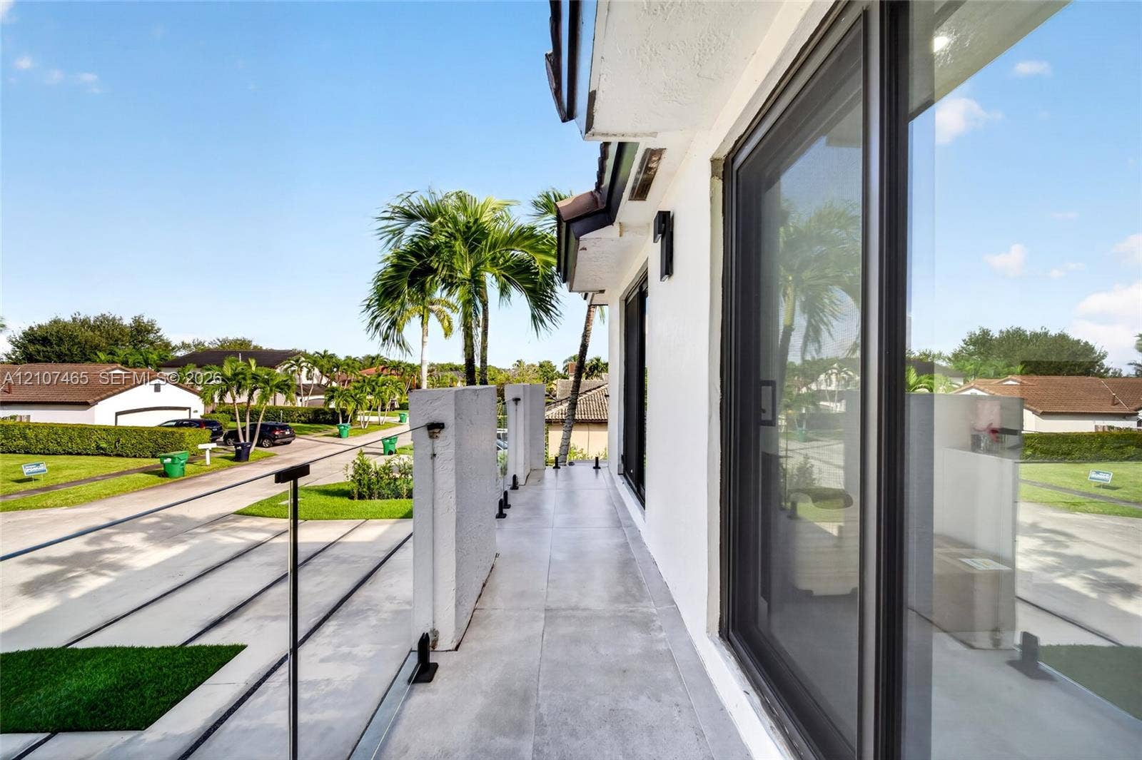 Exterior balcony featuring large-format tile flooring, glass panel railings with metal hardware, and full-height sliding glass doors
