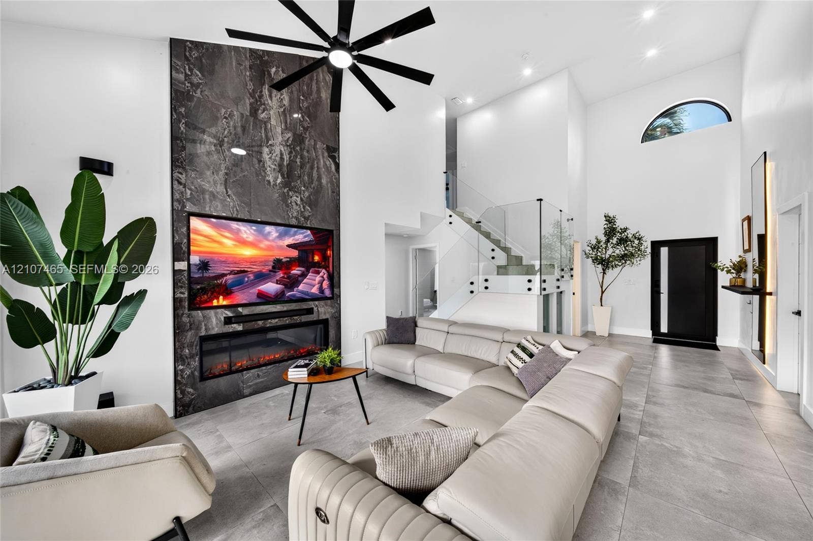 Great room featuring floor-to-ceiling stone fireplace surround, linear electric fireplace, glass staircase railing, tile flooring, and vaulted ceilings with integrated multi-blade ceiling fan