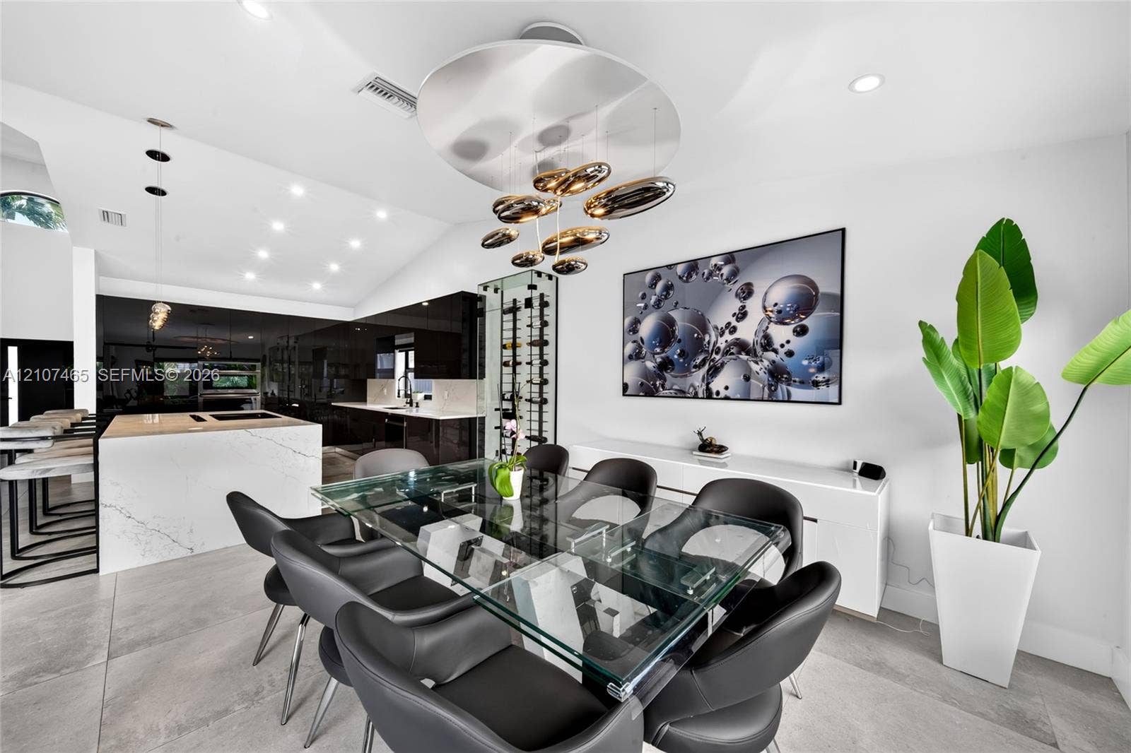 Open-concept space featuring large-format tile flooring, a stone-top kitchen island, recessed lighting, a statement sculptural chandelier, and a built-in vertical wine storage tower