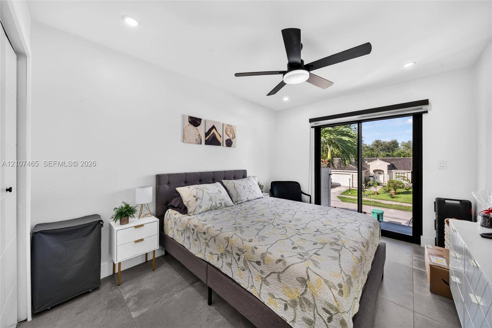 Room featuring large-format tile flooring, matte black ceiling fan with integrated lighting, and sliding glass door with a black frame