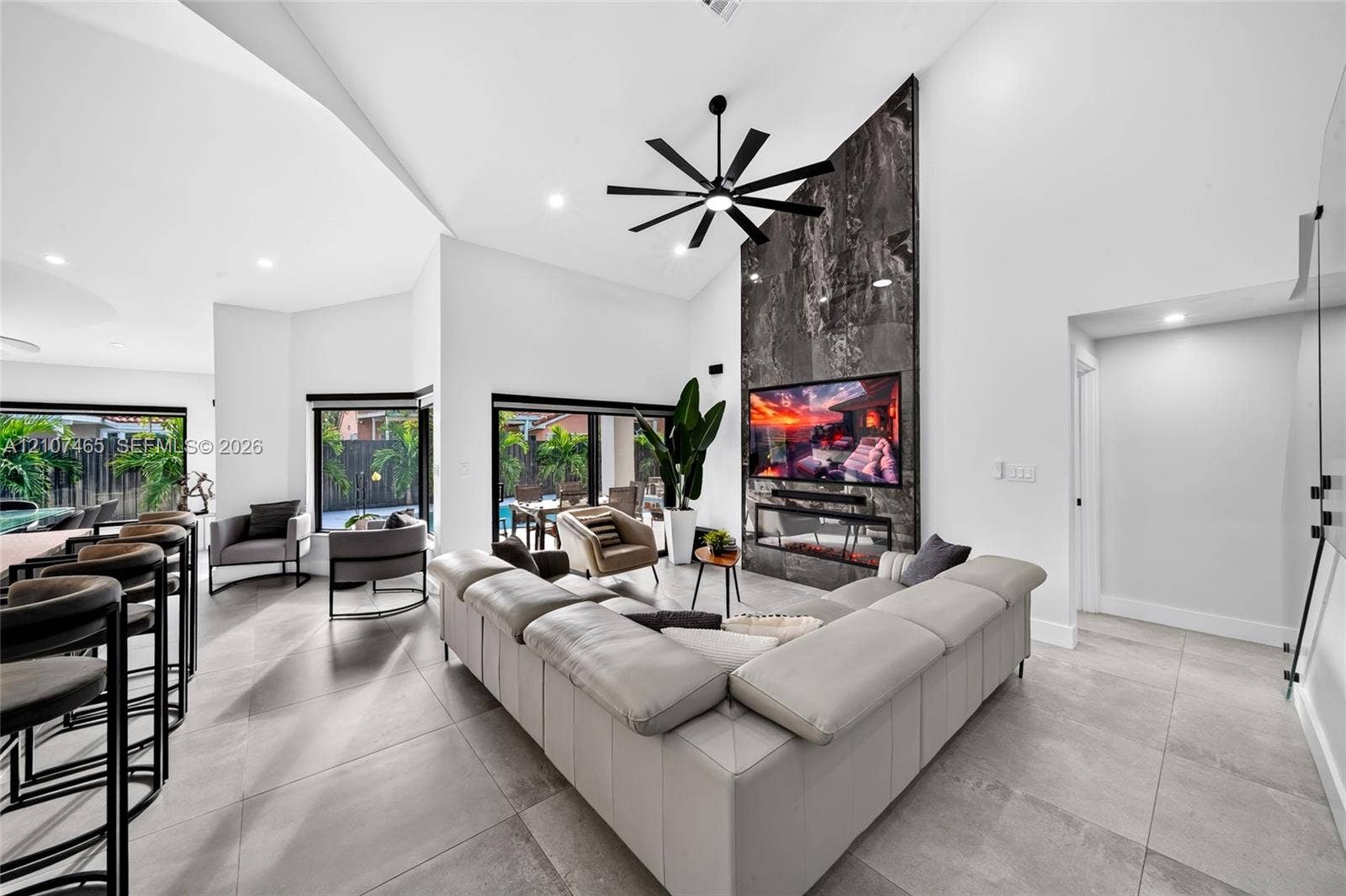 Open-concept living area featuring vaulted ceilings, large-format tile flooring, a floor-to-ceiling stone fireplace surround with a linear electric insert, and sliding glass doors