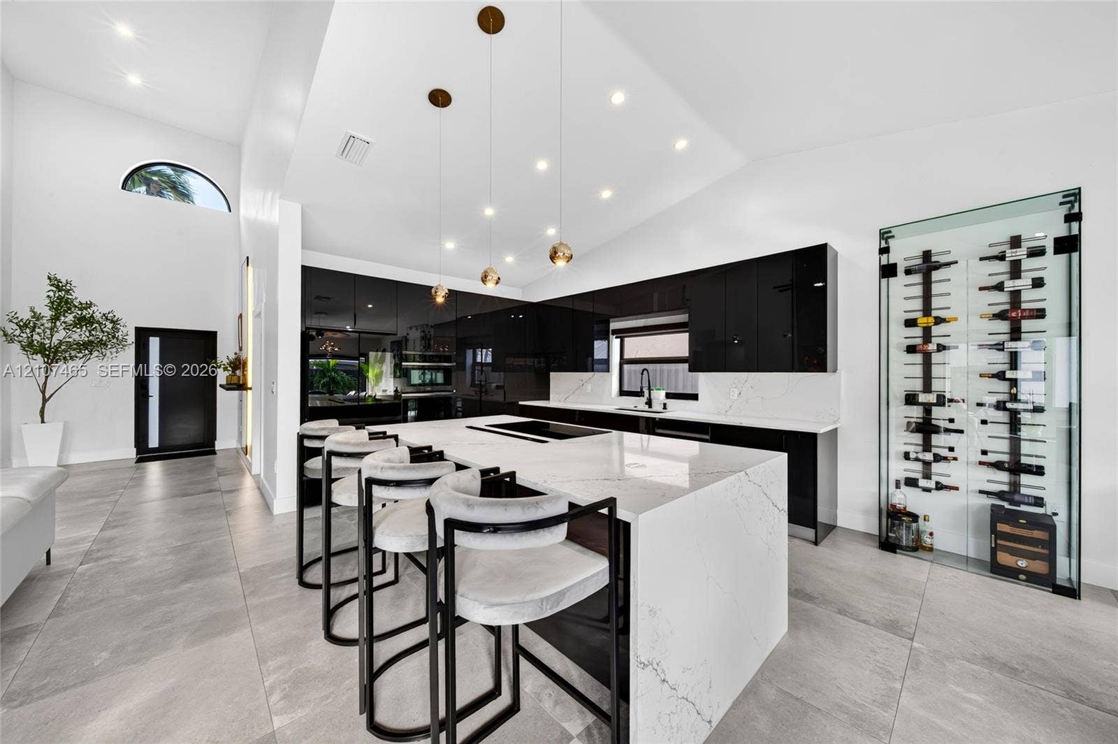 Kitchen featuring a central island with a stone-finish waterfall edge, high-gloss black cabinetry, integrated glass-enclosed wine storage, recessed lighting, and large-format tile flooring