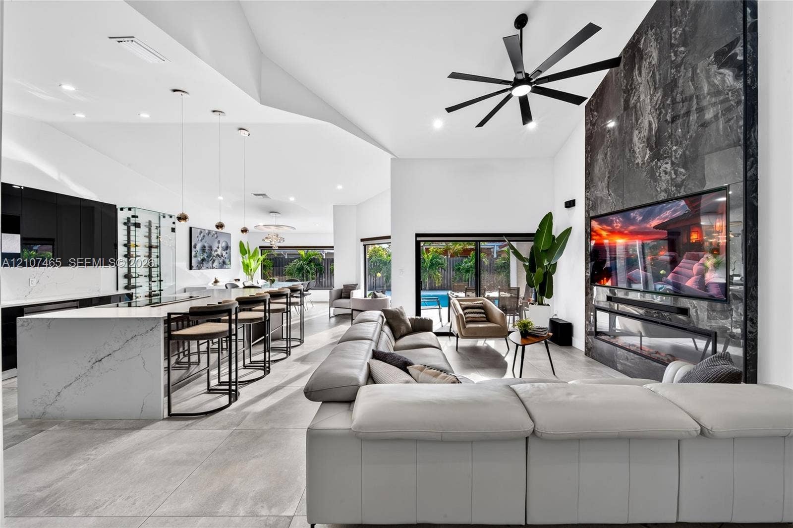 Open-concept kitchen and living area featuring high vaulted ceilings, large-format tile flooring, a kitchen island with quartz countertops, and a floor-to-ceiling stone fireplace surround