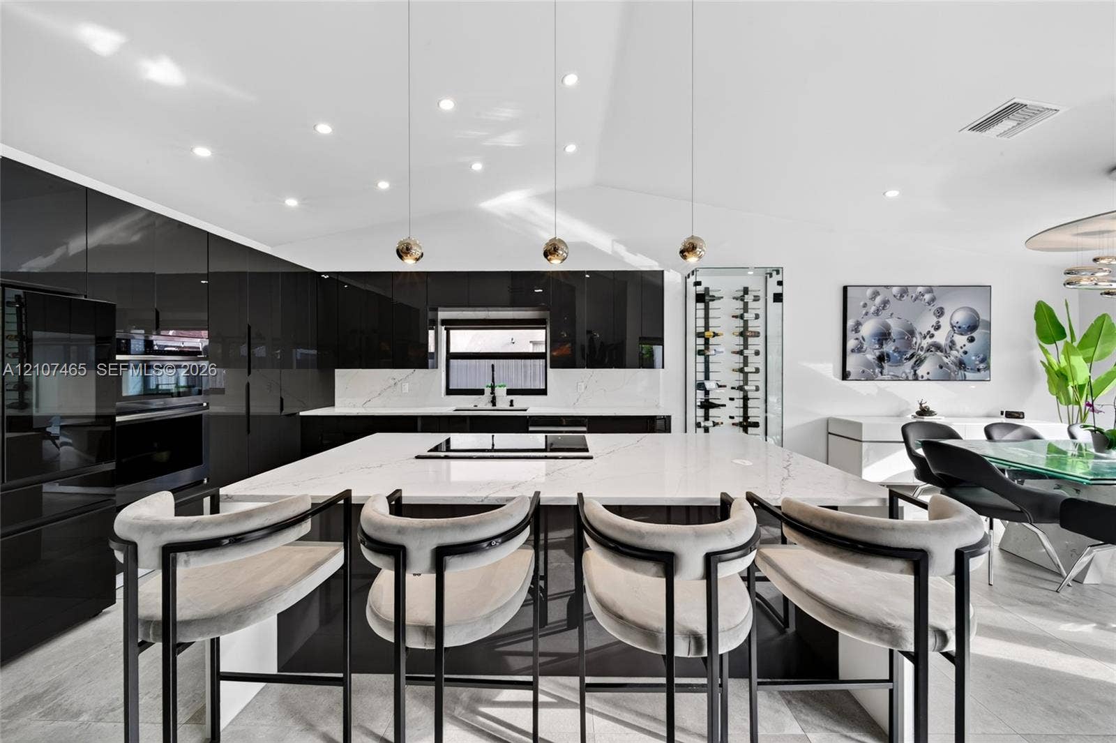High-gloss black cabinetry, expansive central island with stone-finish countertop, integrated wine storage, and three minimalist pendant light fixtures