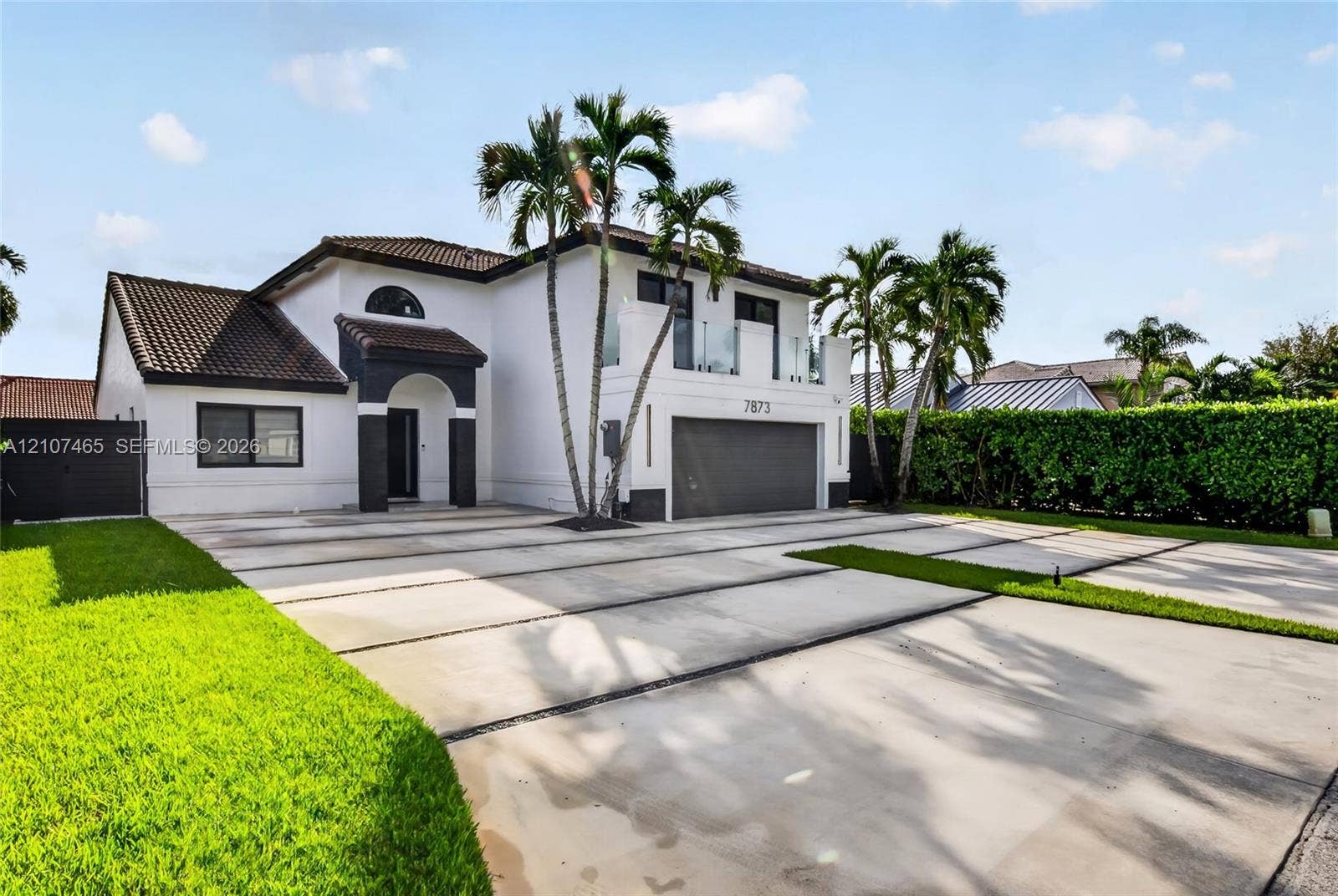 Two-story residence featuring a stucco facade, concrete driveway with grass inlay, attached garage, and an upper-level balcony with glass railings