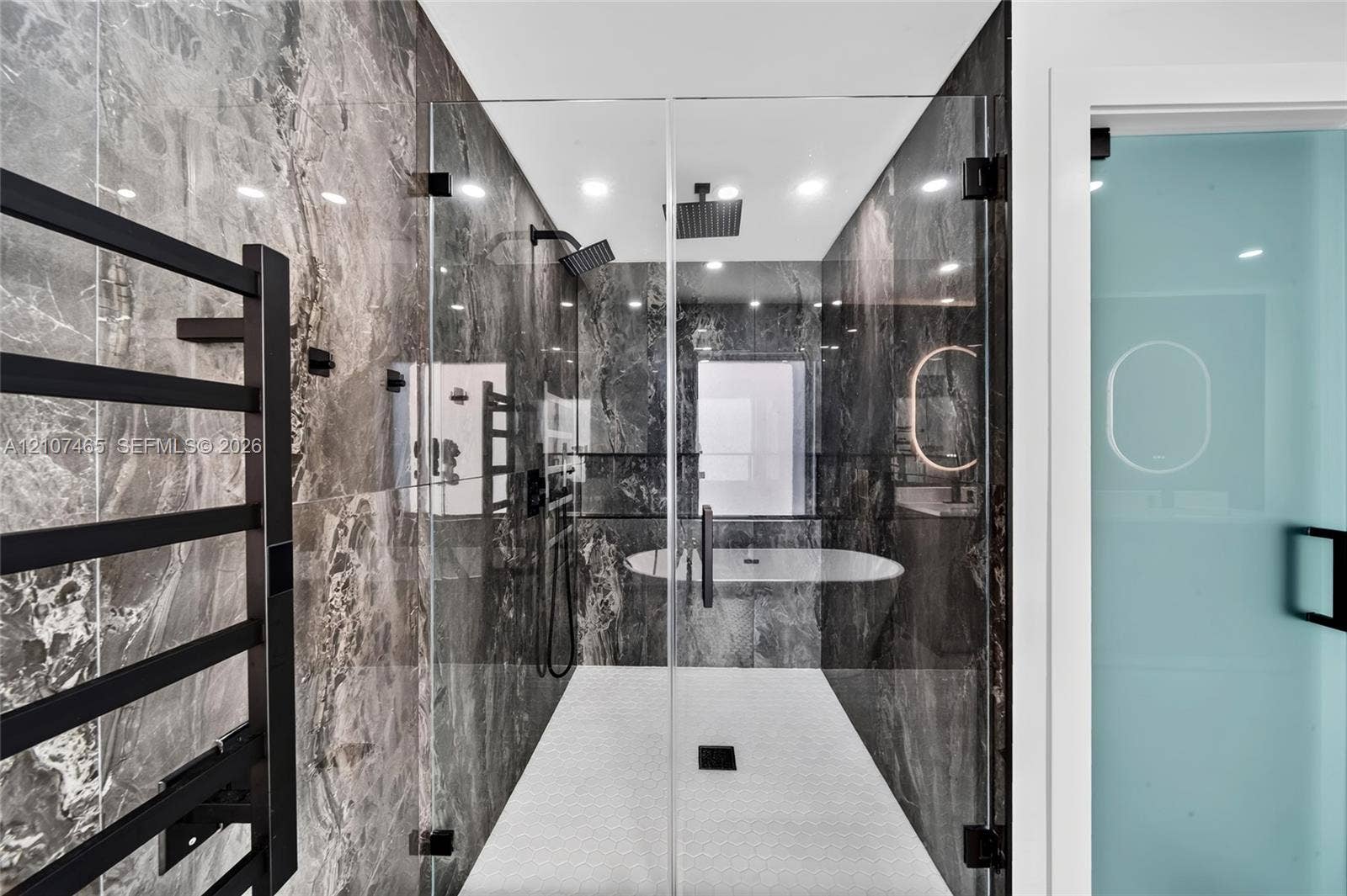 Walk-in shower featuring floor-to-ceiling stone-patterned wall tile, dual rainfall showerheads, a glass enclosure, a freestanding soaking tub, and a matte black wall-mounted towel warmer