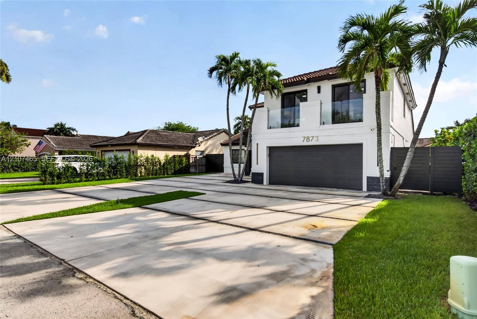 Two-story exterior featuring a smooth stucco facade, dual-car garage with a paneled door, second-story balcony with a glass railing, and a concrete driveway