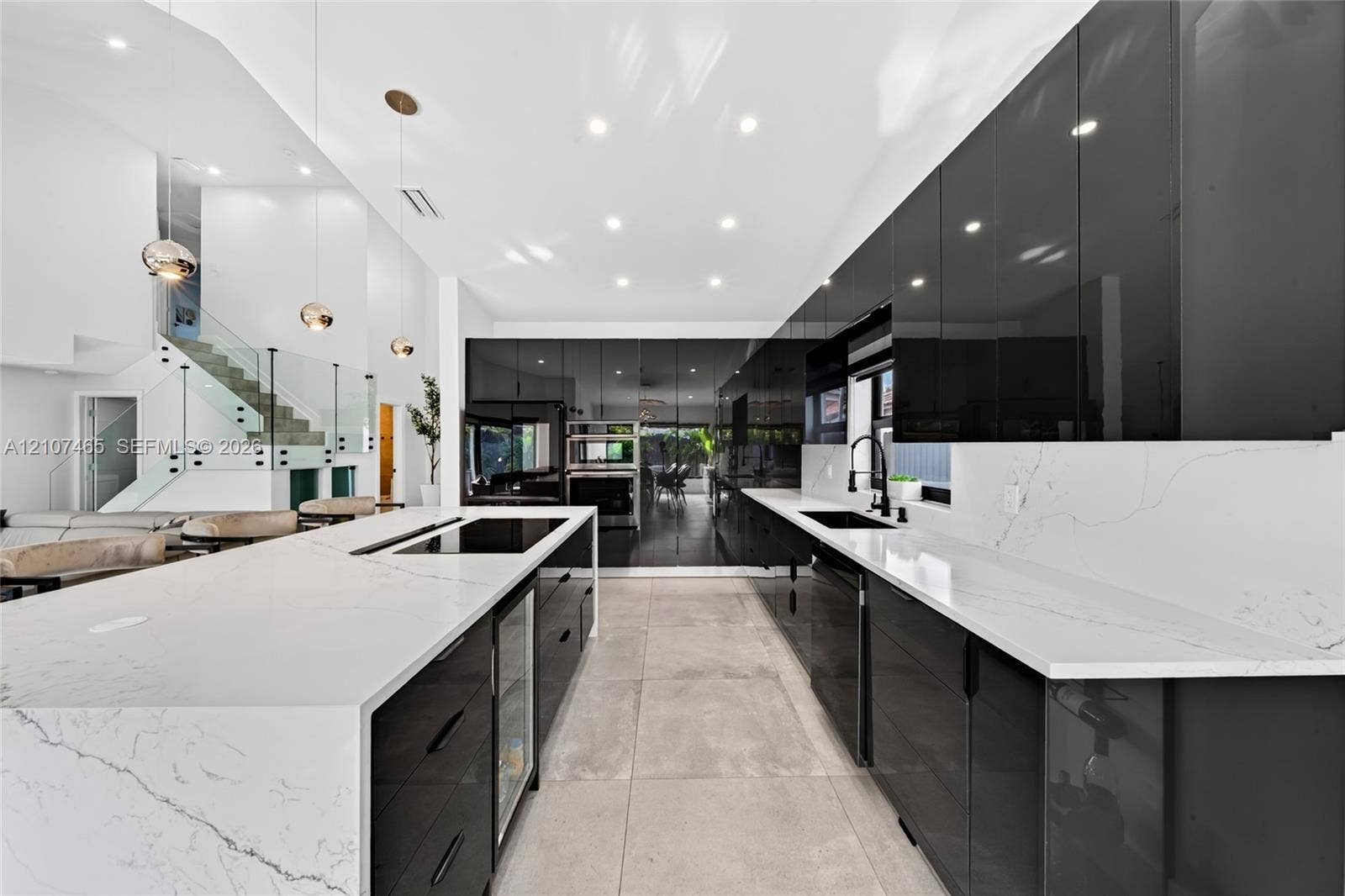 Modern kitchen featuring high-gloss cabinetry, stone-surface countertops with waterfall edge, integrated cooktop, matte black fixtures, and large-format tile flooring