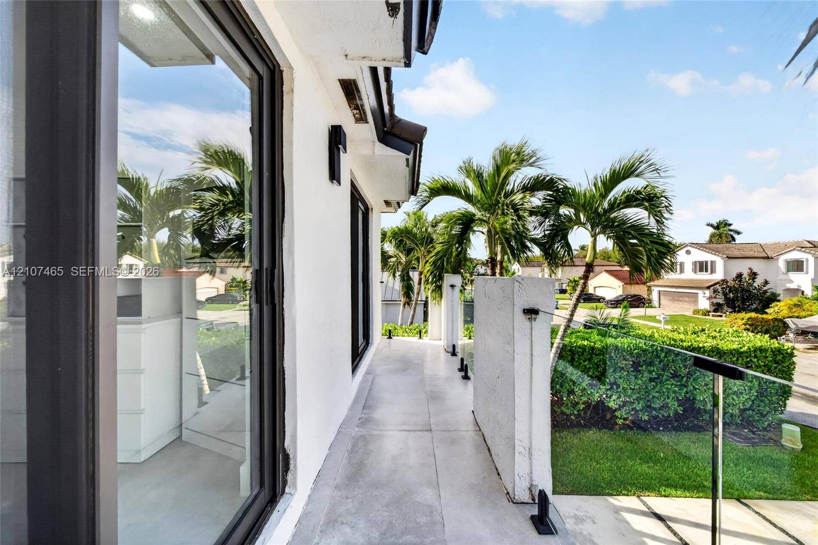 Elevated terrace featuring light-toned tile flooring, clear glass panel railings with metal mounting hardware, and a solid concrete privacy partition