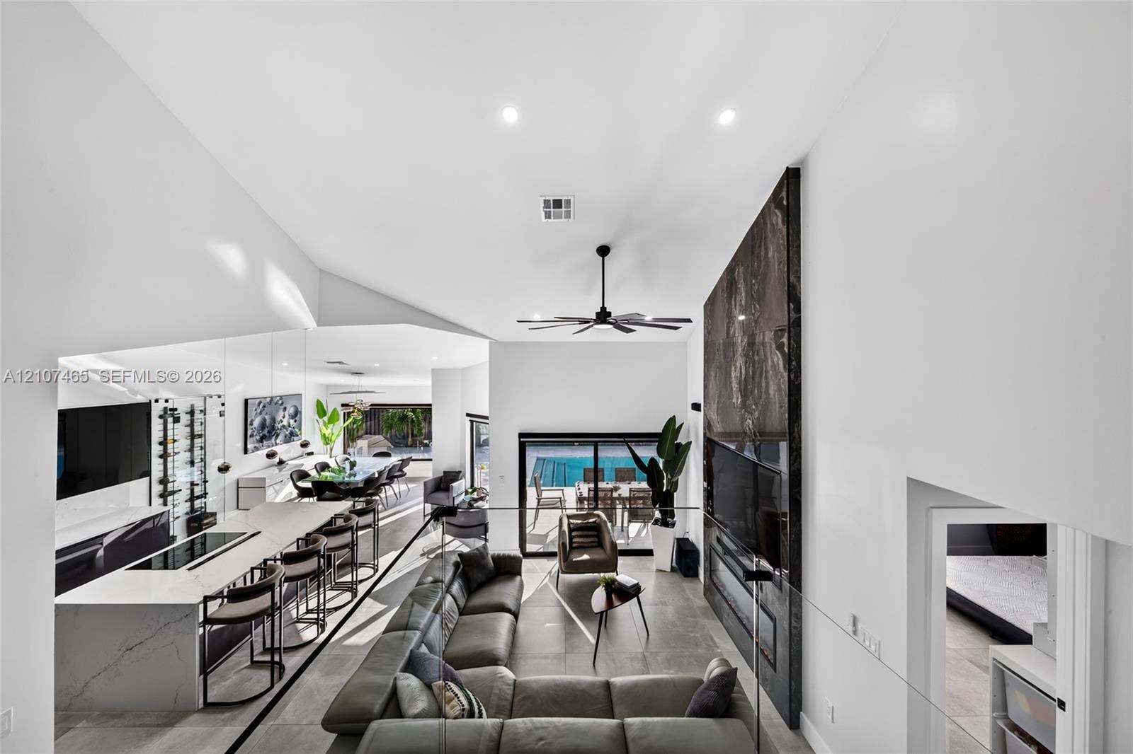 Vaulted ceilings, floor-to-ceiling stone-surround fireplace, large-format tile flooring, built-in wine storage, and quartz-topped island with waterfall edge
