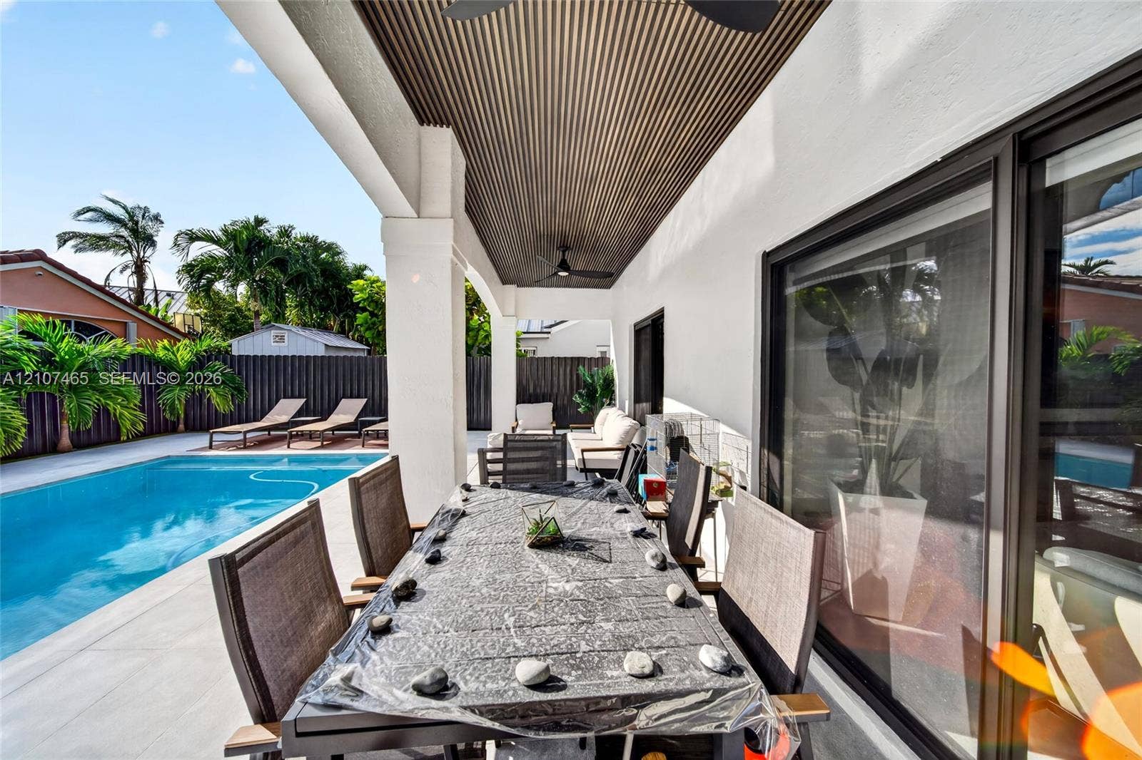 Covered patio featuring a slatted wood-paneled ceiling, recessed ceiling fans, concrete paver decking, and a swimming pool