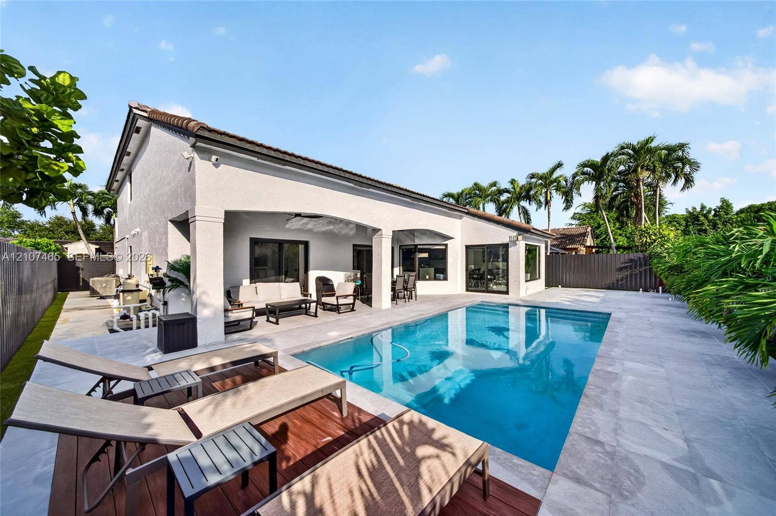 Covered patio featuring architectural arched supports, rectangular in-ground swimming pool, stone-finish patio decking, wood-finish deck inlay, and perimeter fencing