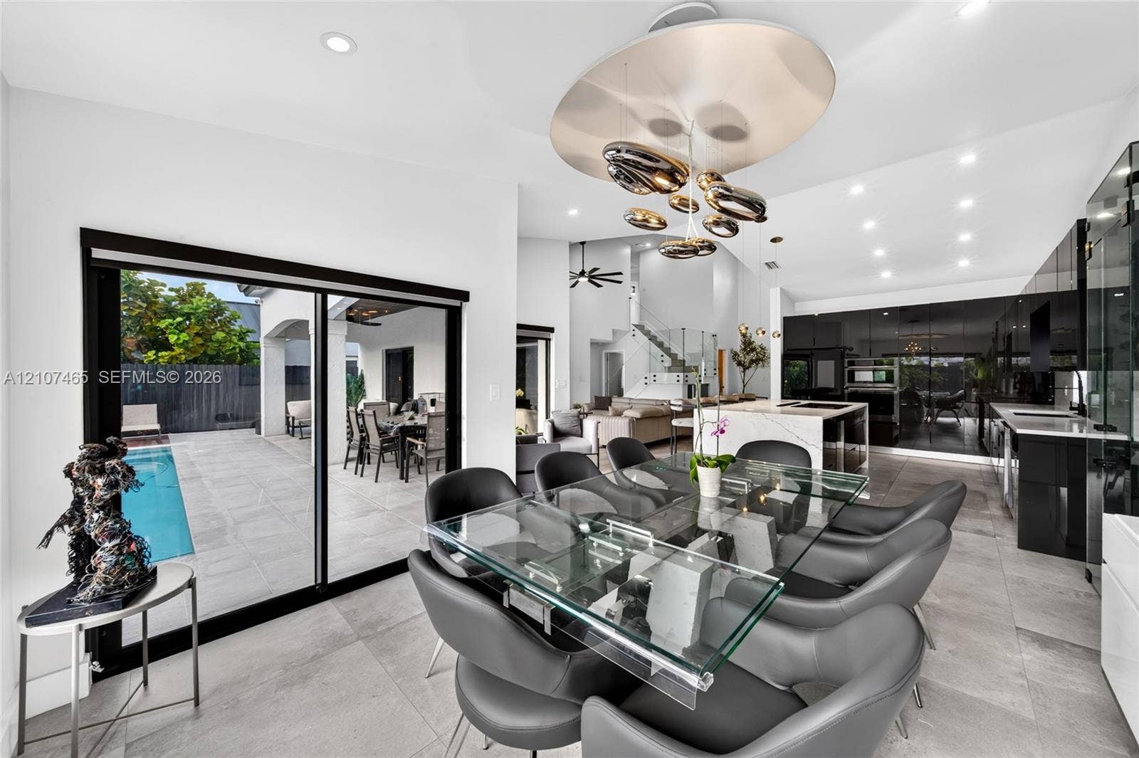 Open-concept space featuring large-format stone tile flooring, high-gloss cabinetry, a central kitchen island with stone countertops, and floor-to-ceiling sliding glass doors