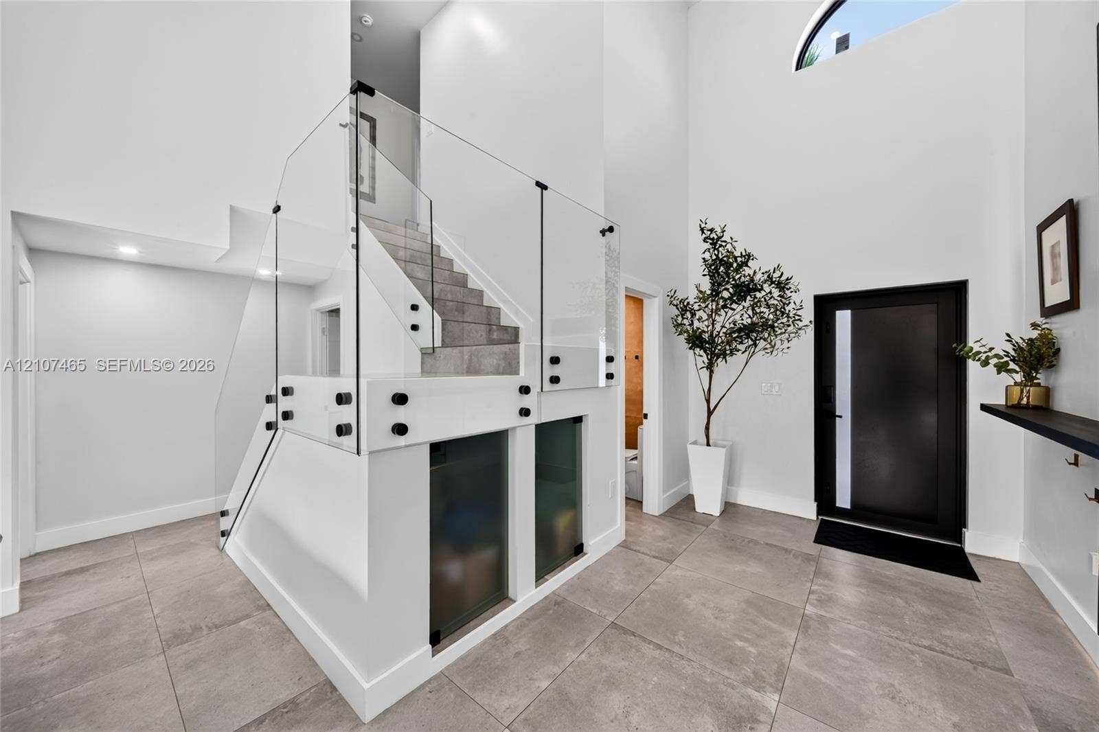 Foyer featuring high ceilings, large-format tile flooring, a glass staircase railing with metal hardware, and a glass-panel entry door