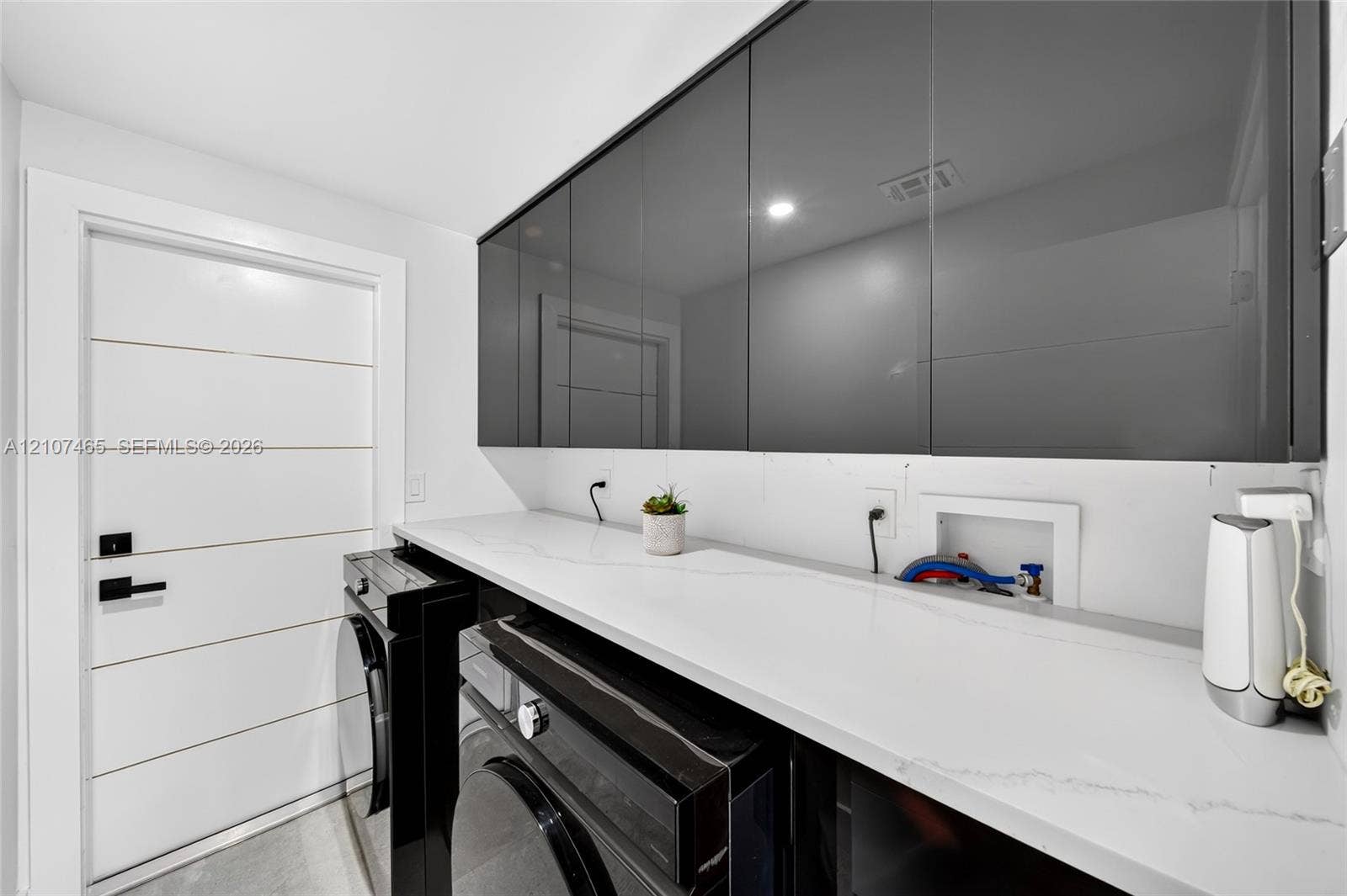 High-gloss dark cabinetry, white stone-finish countertop, recessed lighting, and a multi-panel door with matte black hardware
