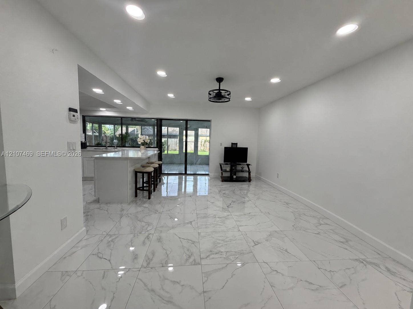 Large-format porcelain tile flooring, recessed ceiling lighting, kitchen island with stone-finish countertop, and black-framed sliding glass doors