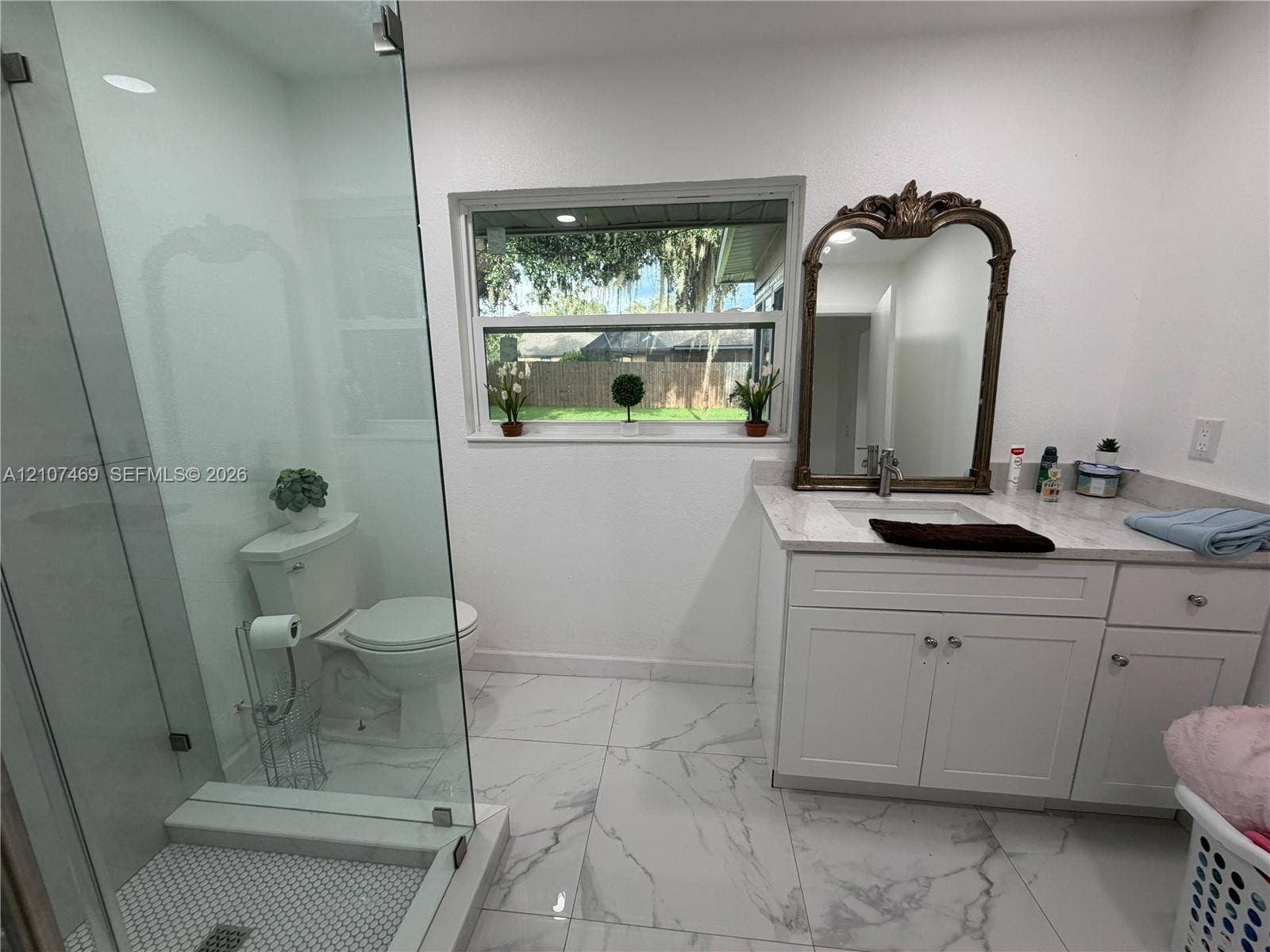 Bathroom featuring large-format tile flooring, a glass-enclosed shower with hexagon mosaic floor tile, white shaker-style cabinetry, and stone-finish countertop