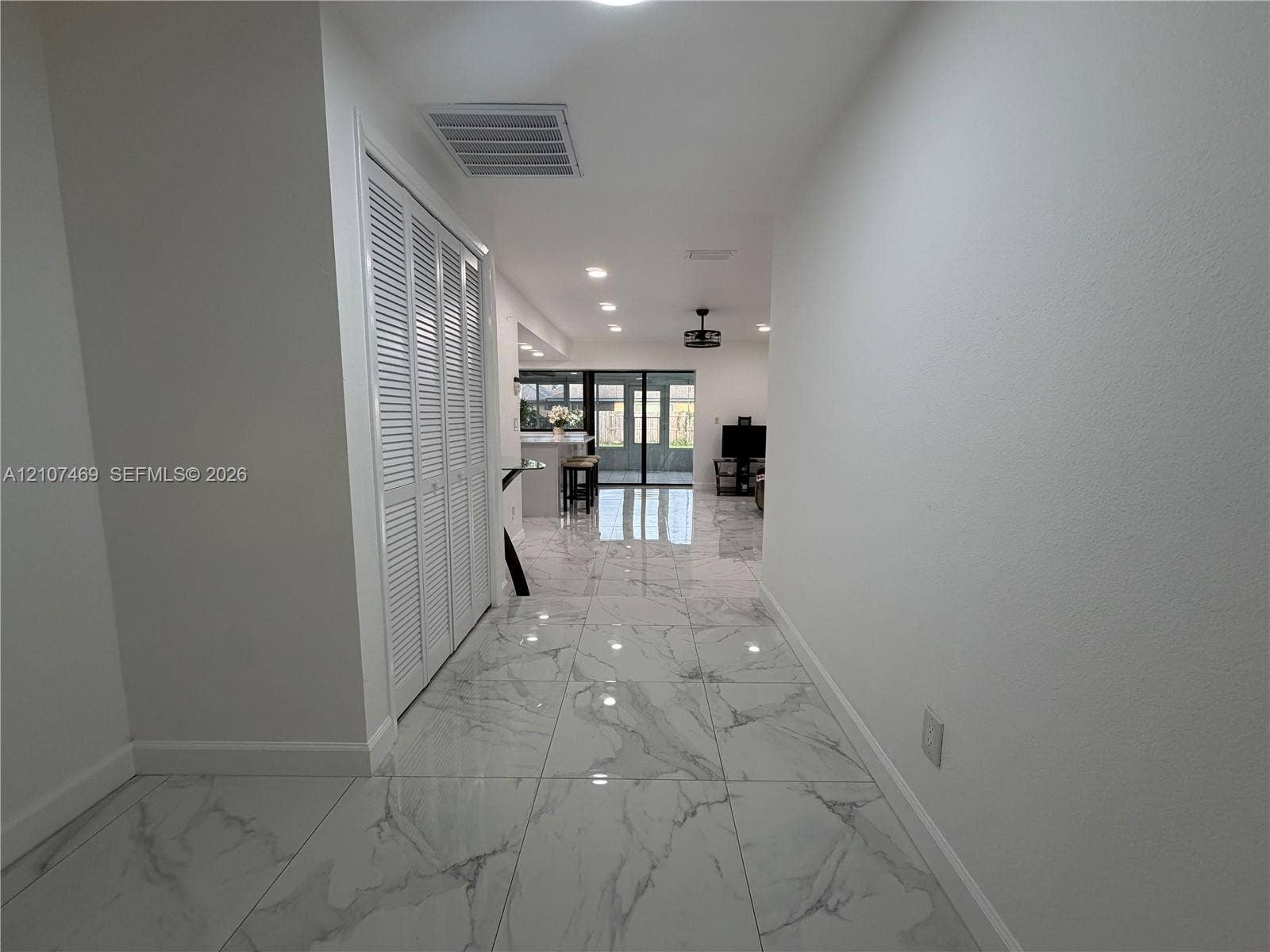 Large-format polished tile flooring, white louvered closet doors, and recessed ceiling lighting
