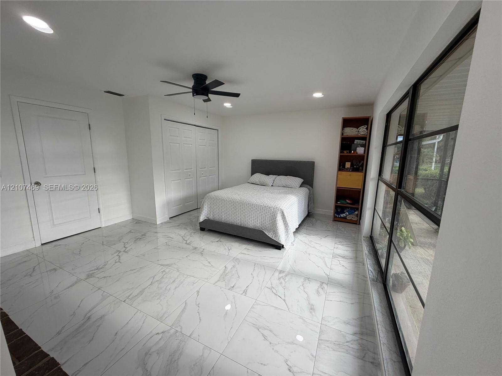 Large-format stone-finish flooring, recessed lighting, ceiling fan with integrated light, and floor-to-ceiling multi-pane windows