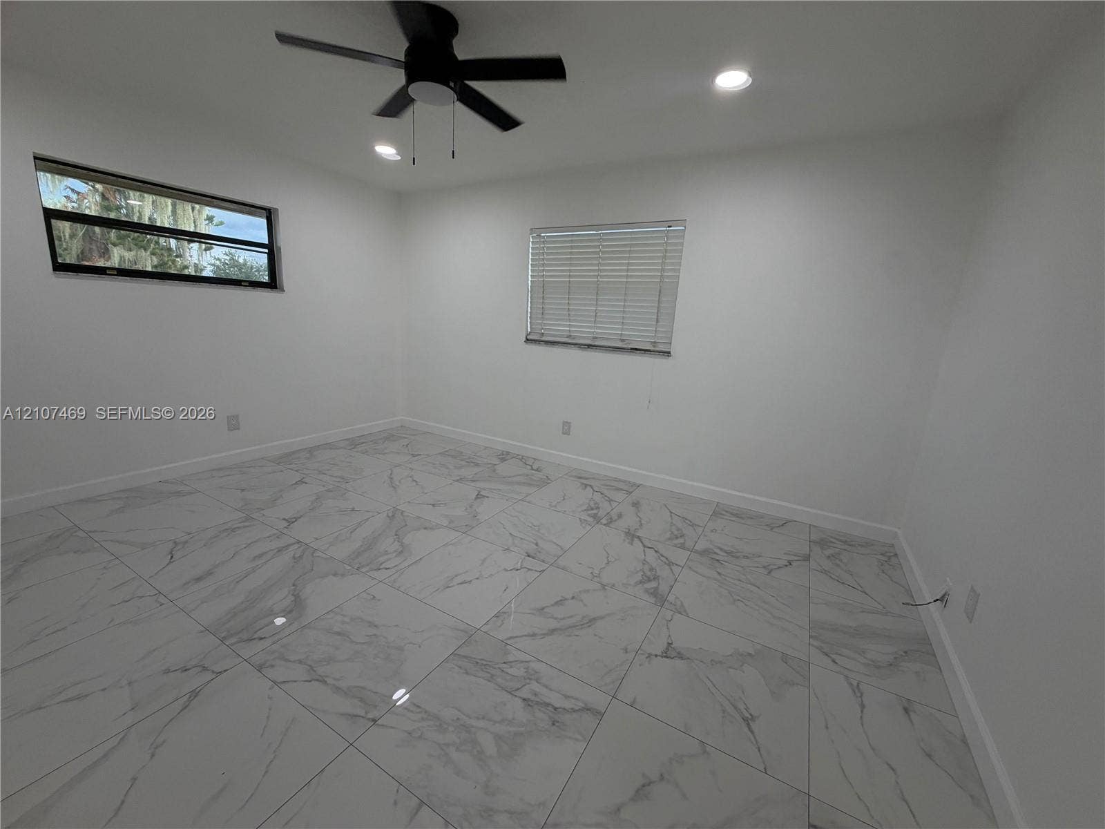 Large-format tile flooring, recessed ceiling lighting, and a modern ceiling fan, punctuated by two windows featuring horizontal blinds