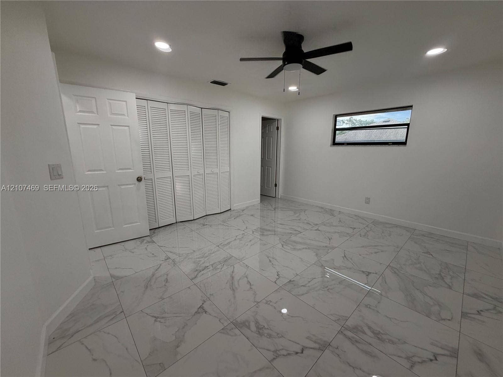 Large-format stone-finish tile flooring, white bi-fold closet doors, recessed ceiling lighting, and a multi-blade ceiling fan