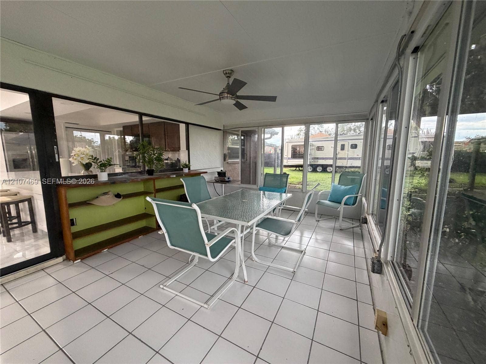 Enclosed sunroom featuring white tile flooring, ceiling fan, and floor-to-ceiling glass panel walls