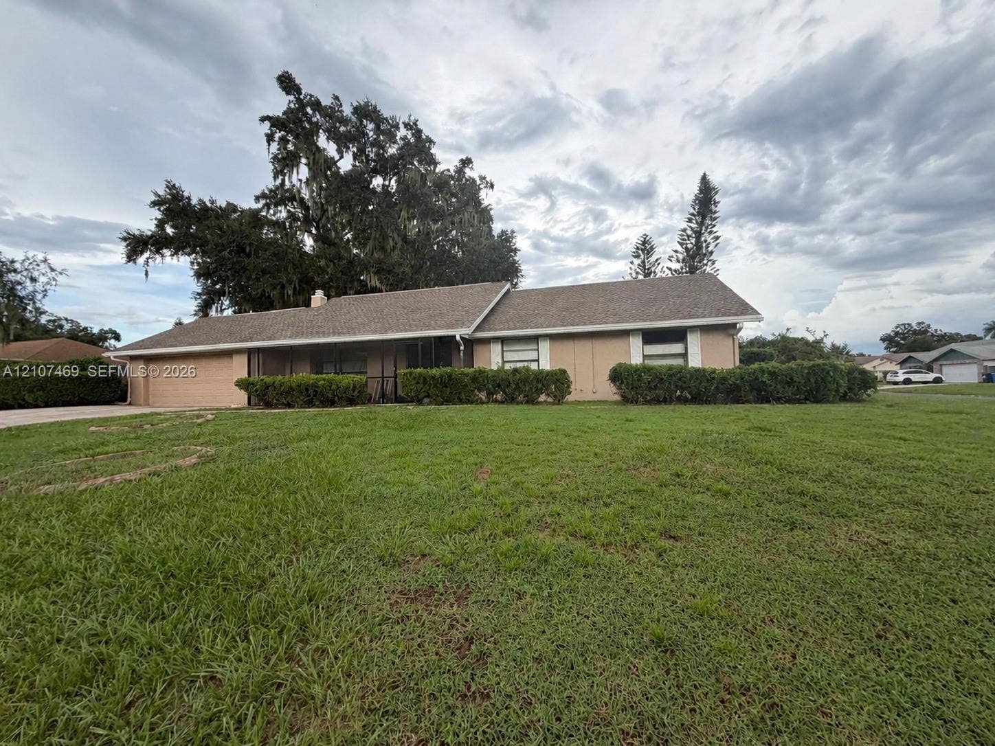 Single-story exterior featuring a shingle roof, integrated garage, screen-enclosed front porch, and mature landscaping