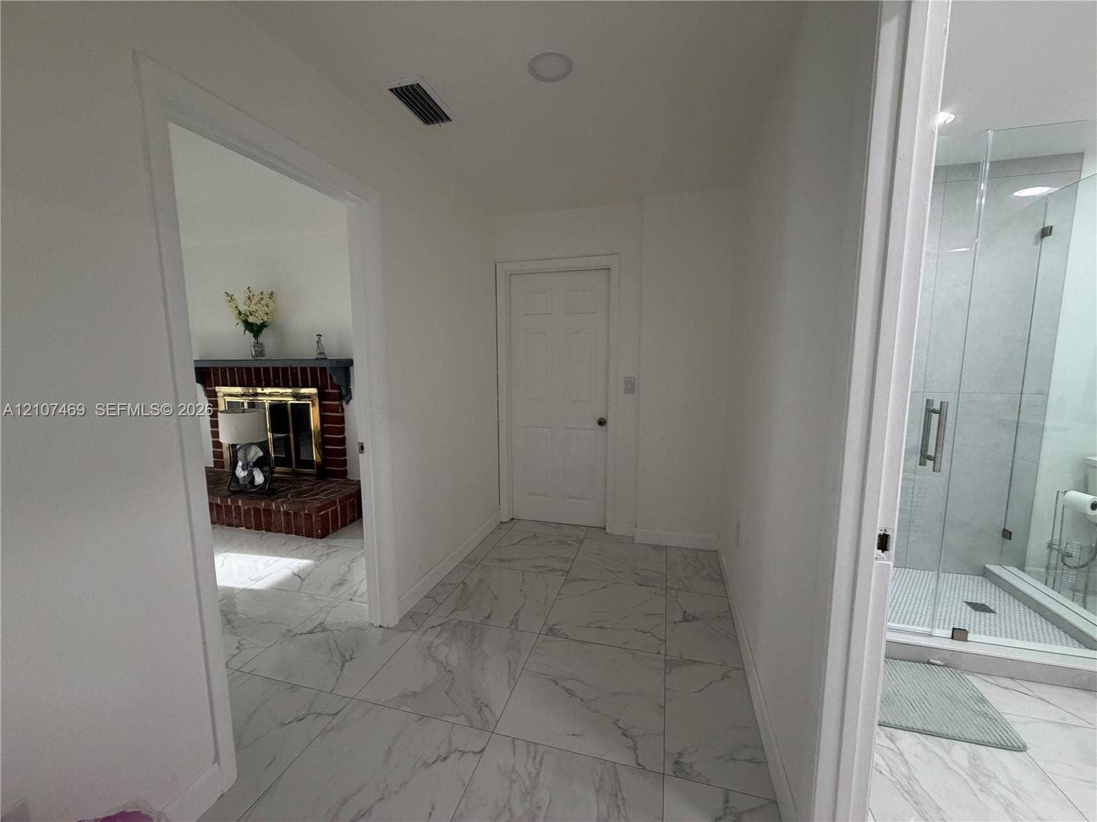 Large-format stone-look tile flooring throughout, walk-in shower with glass enclosure, and brick fireplace with mantle