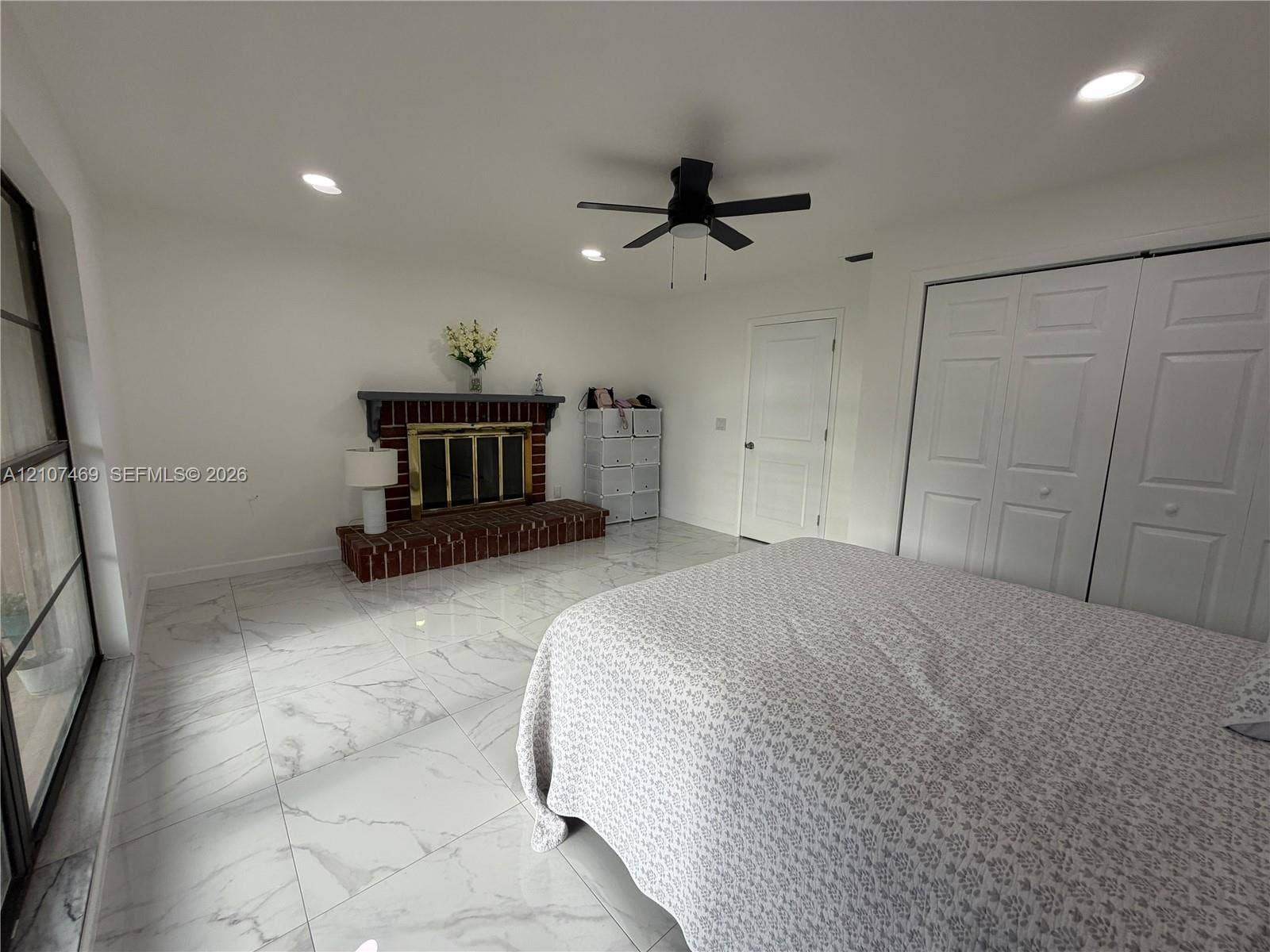 Room featuring large-format tile flooring, a brick fireplace with a mantle, recessed ceiling lighting, a ceiling fan, and double-door closets