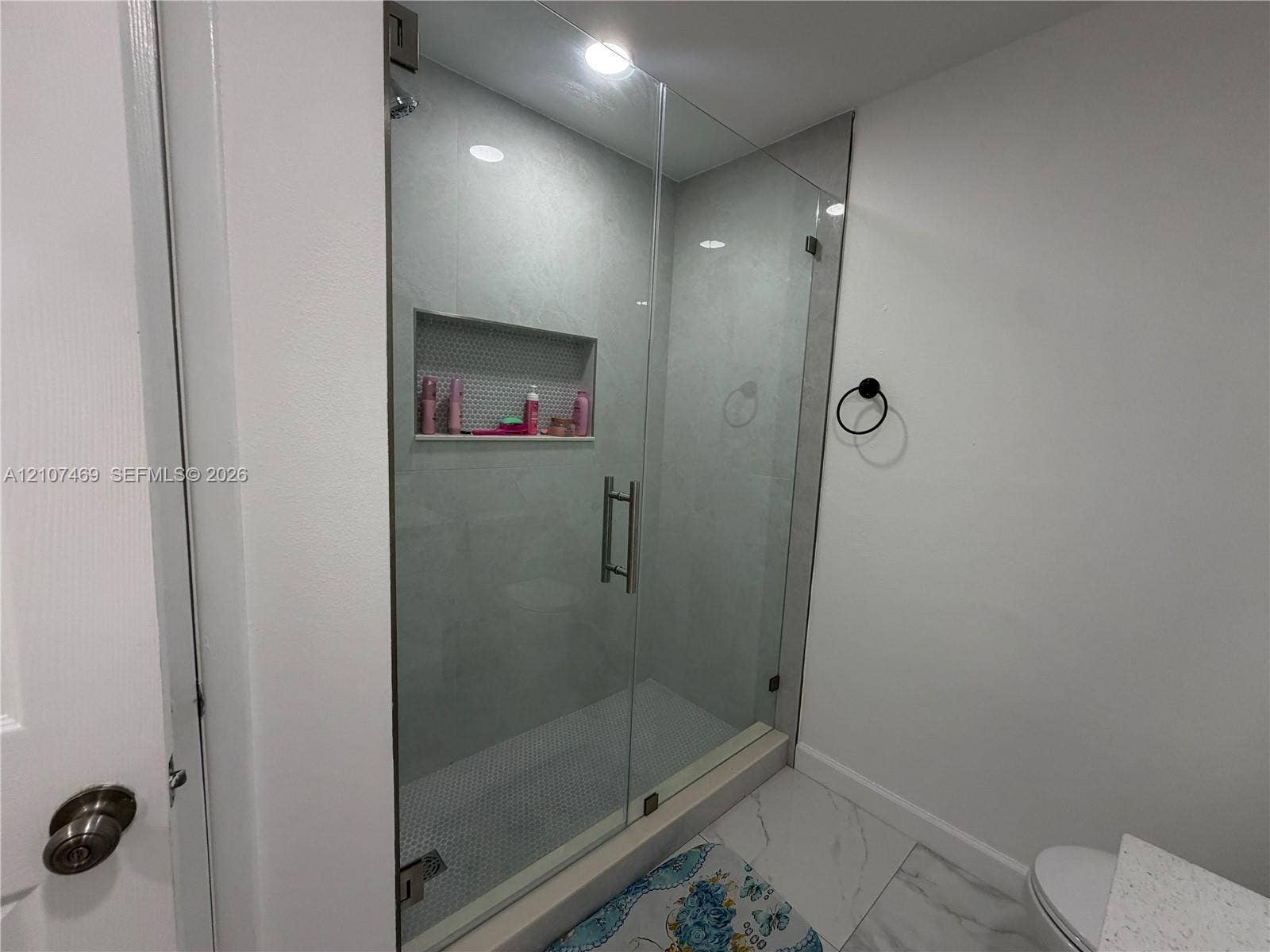 Walk-in shower with a frameless glass door, light-toned wall tile, hexagonal tile floor inlay, and a built-in recessed wall niche