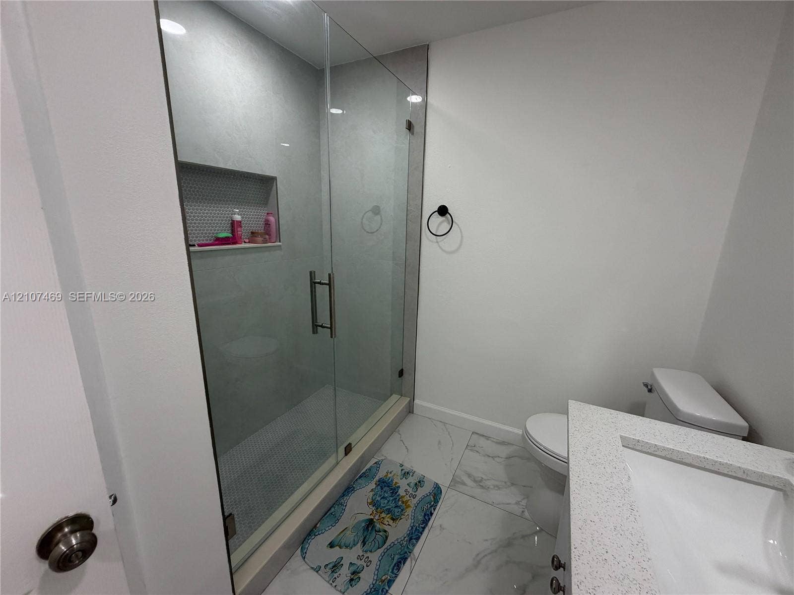 Walk-in shower with a glass enclosure, built-in tiled niche, stone-look tile flooring, and vanity with a rectangular sink and composite countertop