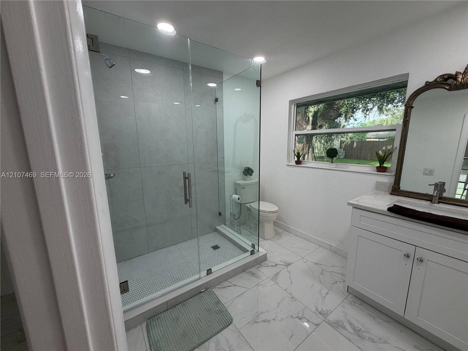 Walk-in shower featuring glass paneling and large-format tile surround, white cabinetry with countertop, and large-format flooring