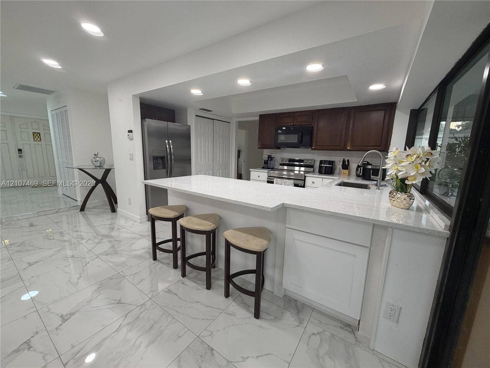Kitchen featuring a quartz countertop island with a breakfast bar, stone-finish tile flooring, recessed lighting, and stainless steel appliances