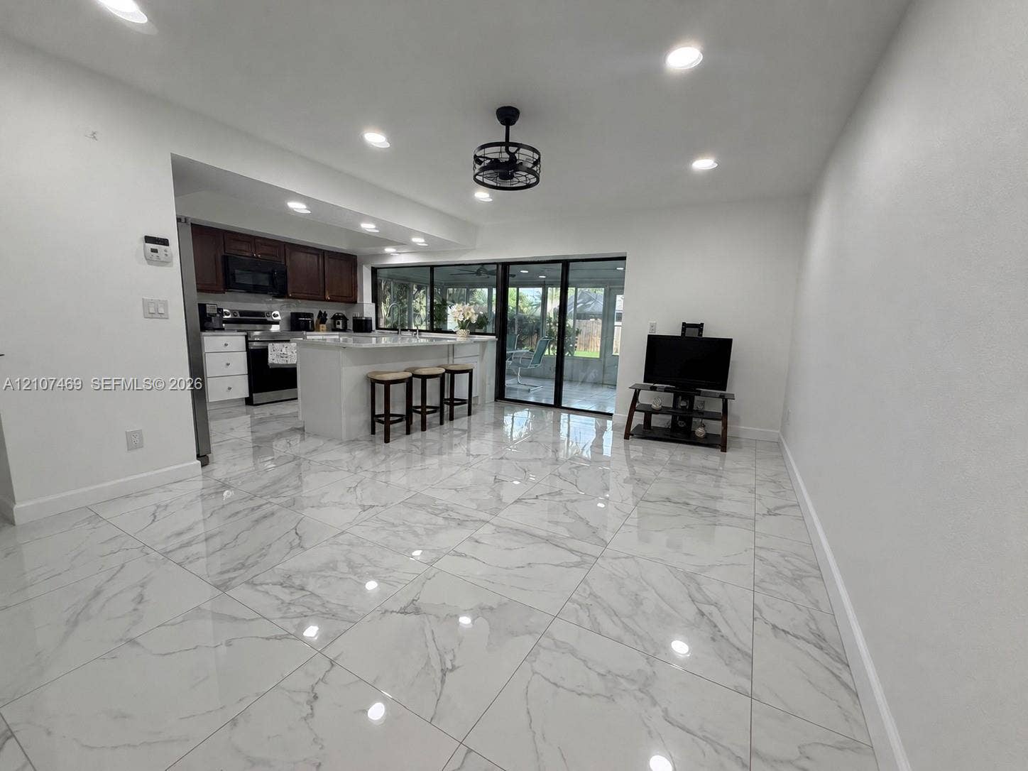 Large-format tile flooring with a marble-pattern finish, recessed ceiling lighting, industrial-style drum ceiling fan, kitchen island with a white countertop, and expansive sliding glass doors