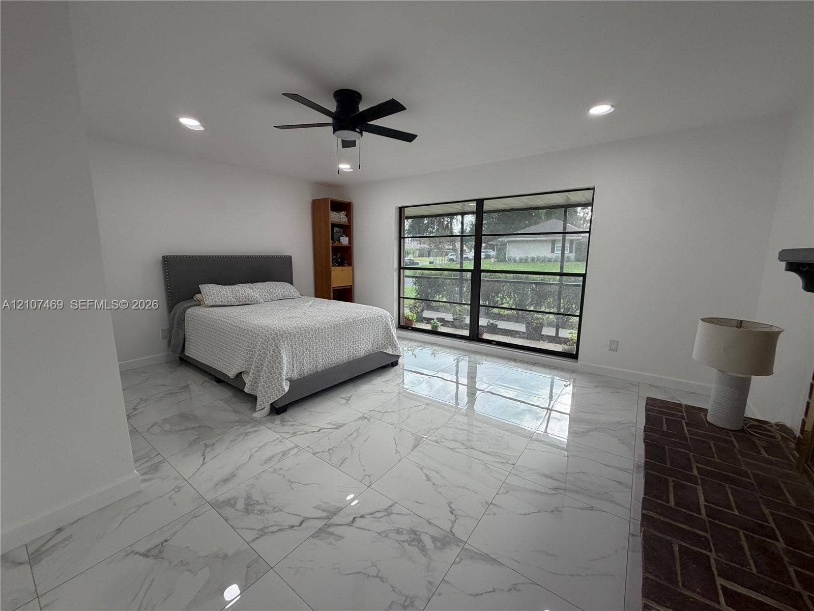 Large-format polished tile flooring, black-framed floor-to-ceiling windows, recessed lighting, matte black ceiling fan, and herringbone-patterned brick fireplace surround