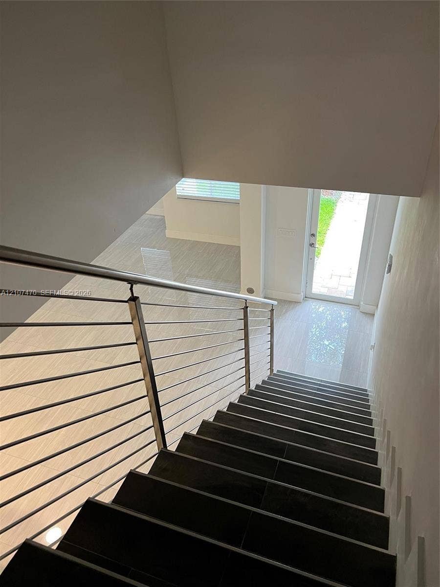 1629 NE 9th Street, #1629, Fort Lauderdale, Fort Lauderdale, FL 33304 Staircase featuring dark tile treads, a stainless steel cable railing system, polished large-format floor tile, and a glass-paneled entry door