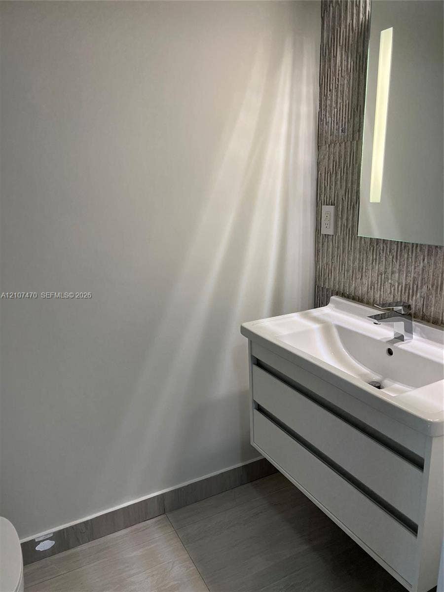 1629 NE 9th Street, #1629, Fort Lauderdale, Fort Lauderdale, FL 33304 Floating white vanity with dual drawers, integrated sink, chrome faucet, textured stone-finish backsplash, and vertical wall-mounted mirror