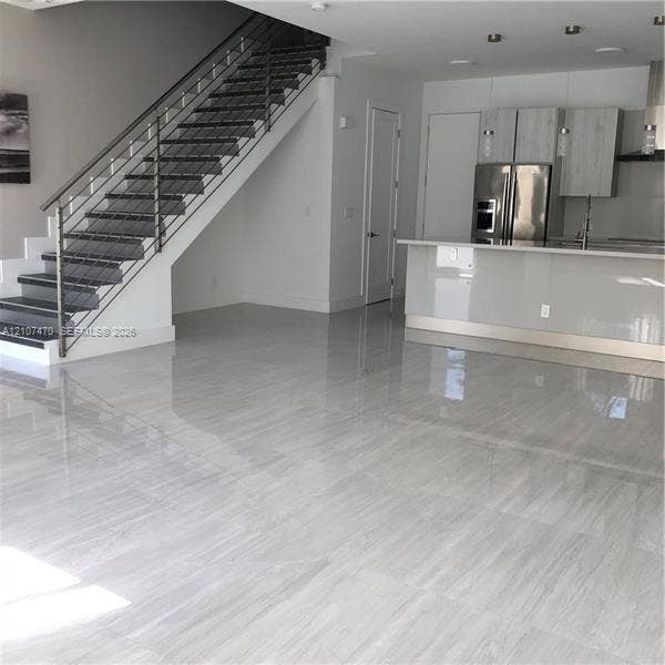 1629 NE 9th Street, #1629, Fort Lauderdale, Fort Lauderdale, FL 33304 Open-concept interior featuring large-format tile flooring, a modern staircase with a metal cable railing, flat-panel cabinetry, a kitchen island with a stone-finish countertop, and stainless steel appliances