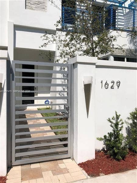 1629 NE 9th Street, #1629, Fort Lauderdale, Fort Lauderdale, FL 33304 Contemporary exterior featuring a gated entry with horizontal metal slats, stone paver walkway, stucco finish wall, and geometric wall-mounted lighting