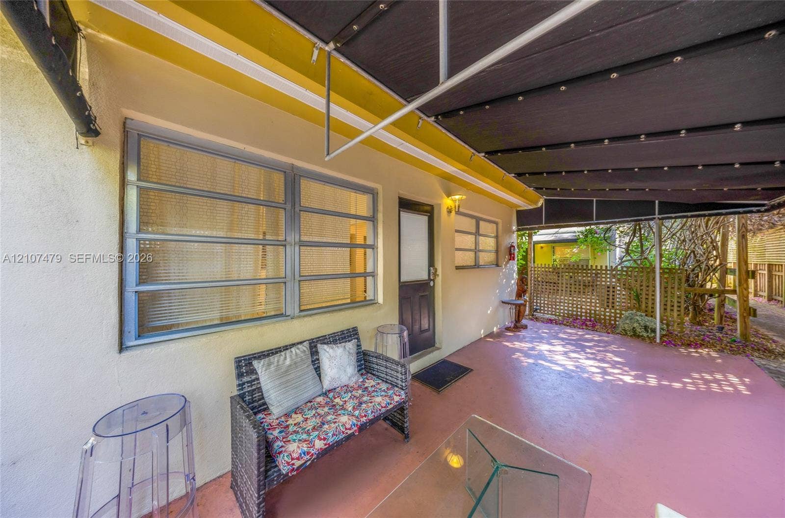 Covered outdoor patio with a concrete floor, retractable black fabric awning, jalousie-style windows, and a solid-panel exterior door with glass insert