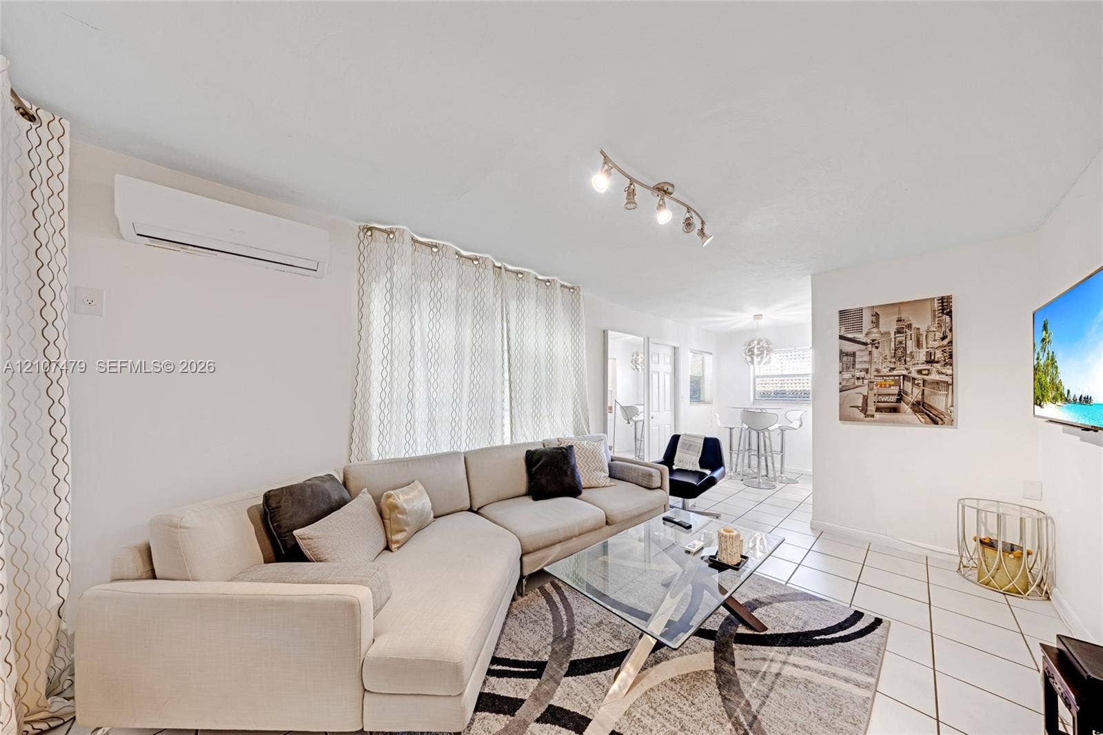 Main living area featuring tile flooring, a wall-mounted ductless air conditioning unit, and directional track lighting