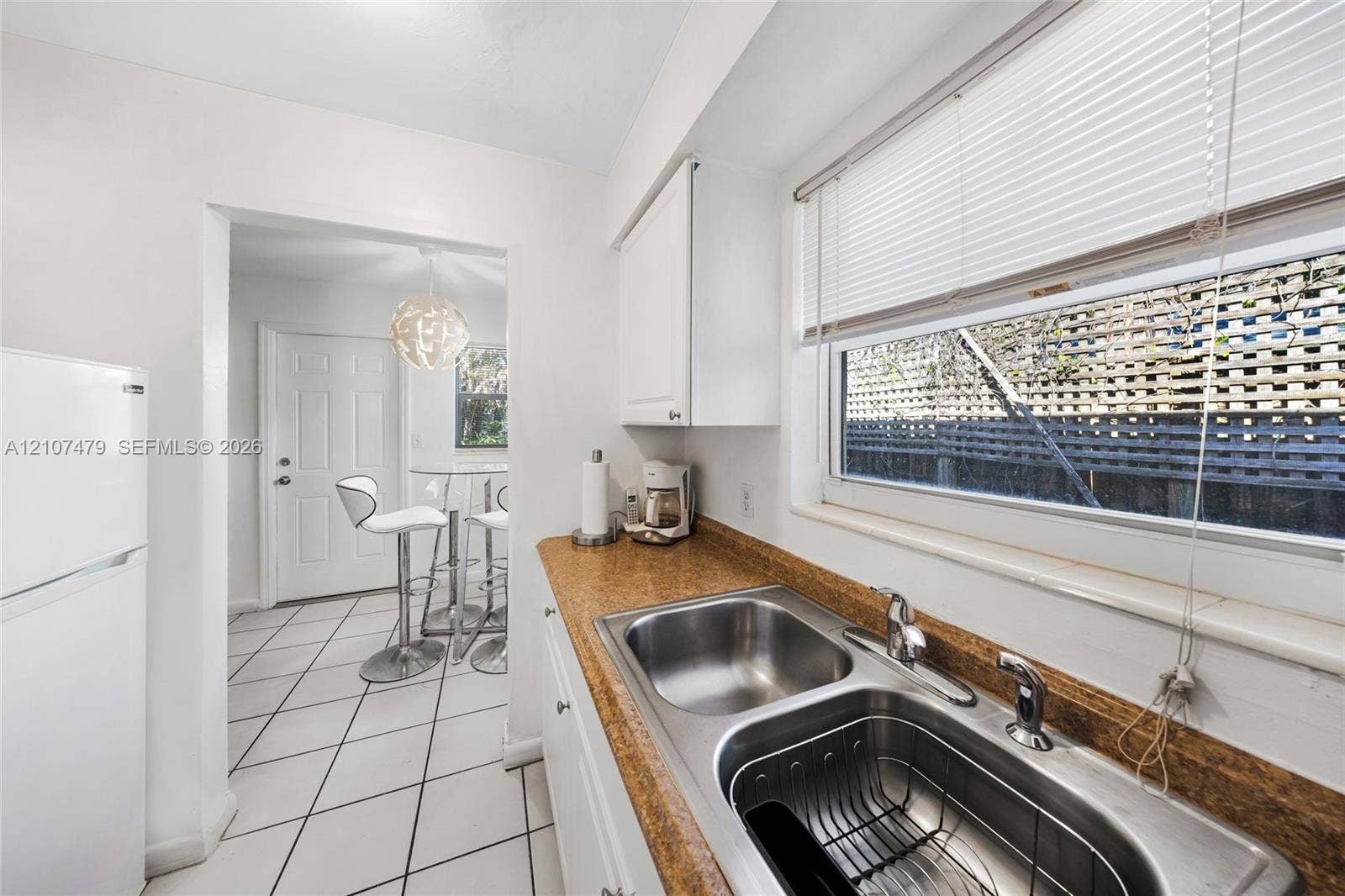 Kitchen featuring white cabinetry, stone-finish countertops, a double-basin stainless steel sink with a high-arch faucet, and tile flooring