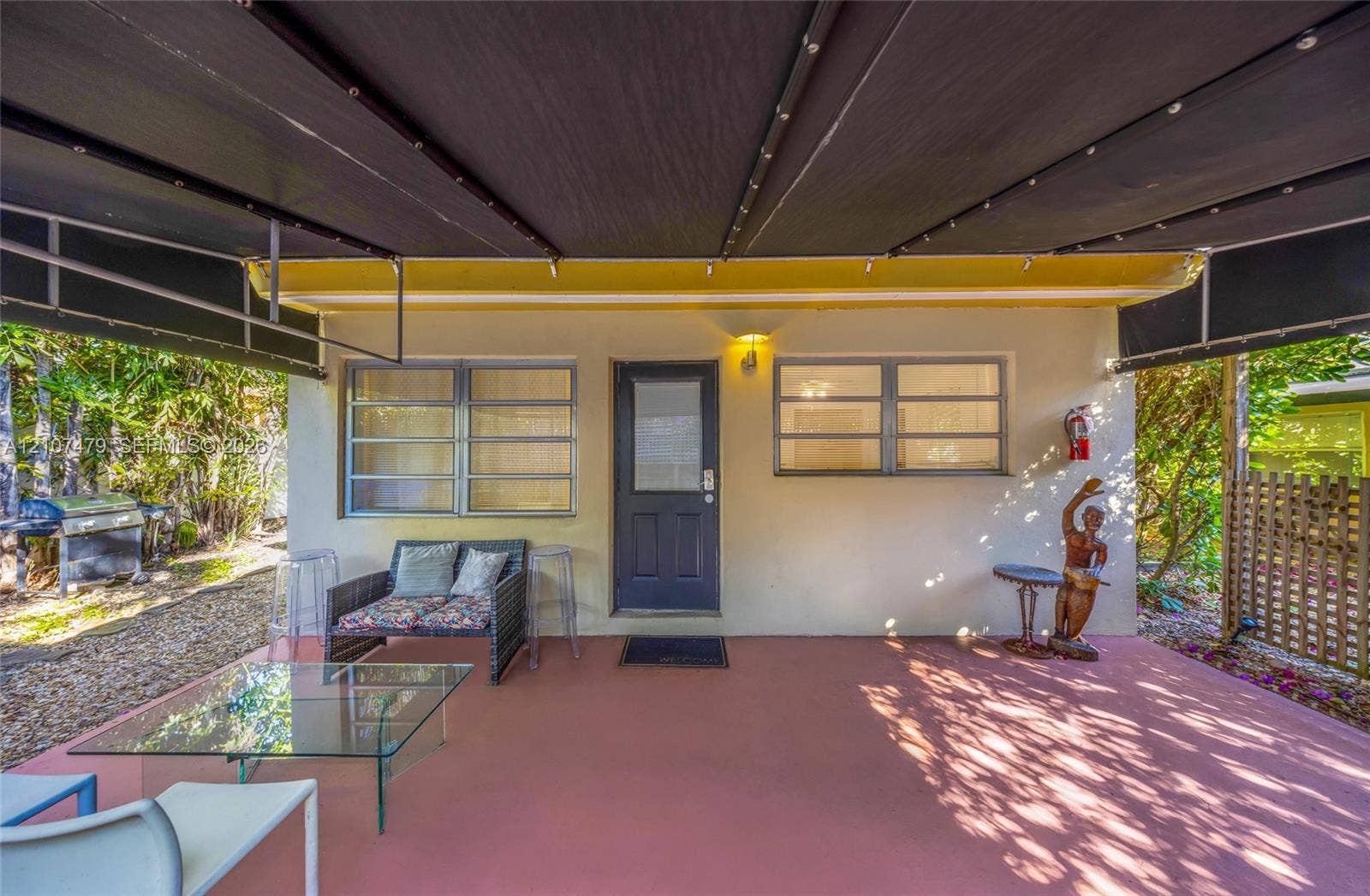 Covered patio featuring a solid-surface floor, retractable black fabric awning, horizontal sliding windows, and a glass-paneled exterior door