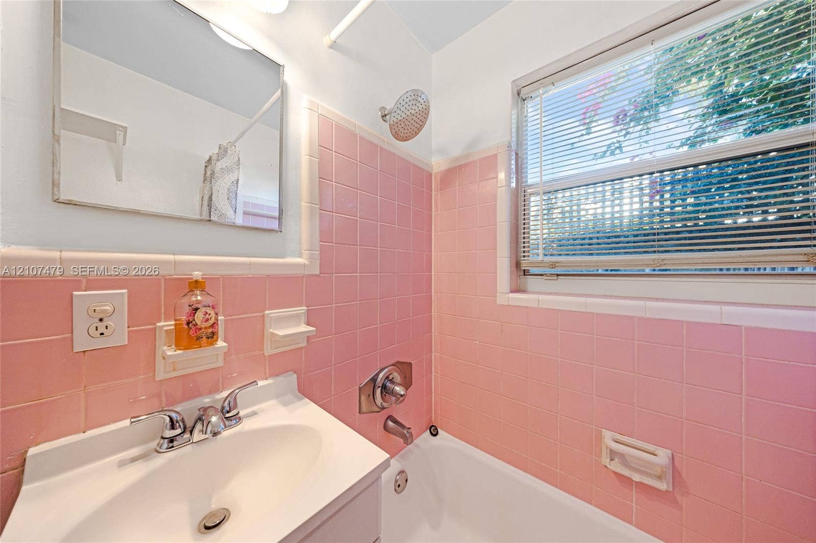 Bathroom featuring pink ceramic wall tiling, a white porcelain sink with a polished chrome widespread faucet, a wall-mounted medicine cabinet, and a shower-tub combination with a chrome showerhead