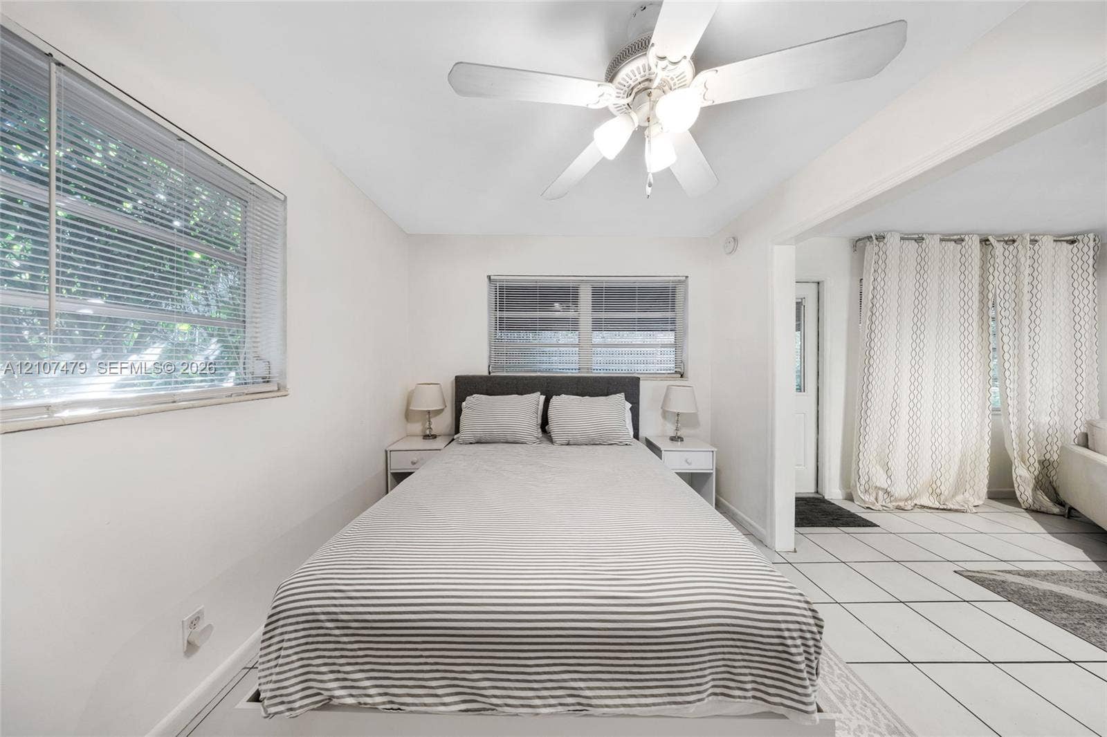 Neutral-toned room featuring a white ceiling fan with integrated lighting, dual horizontal windows, and large-format tile flooring
