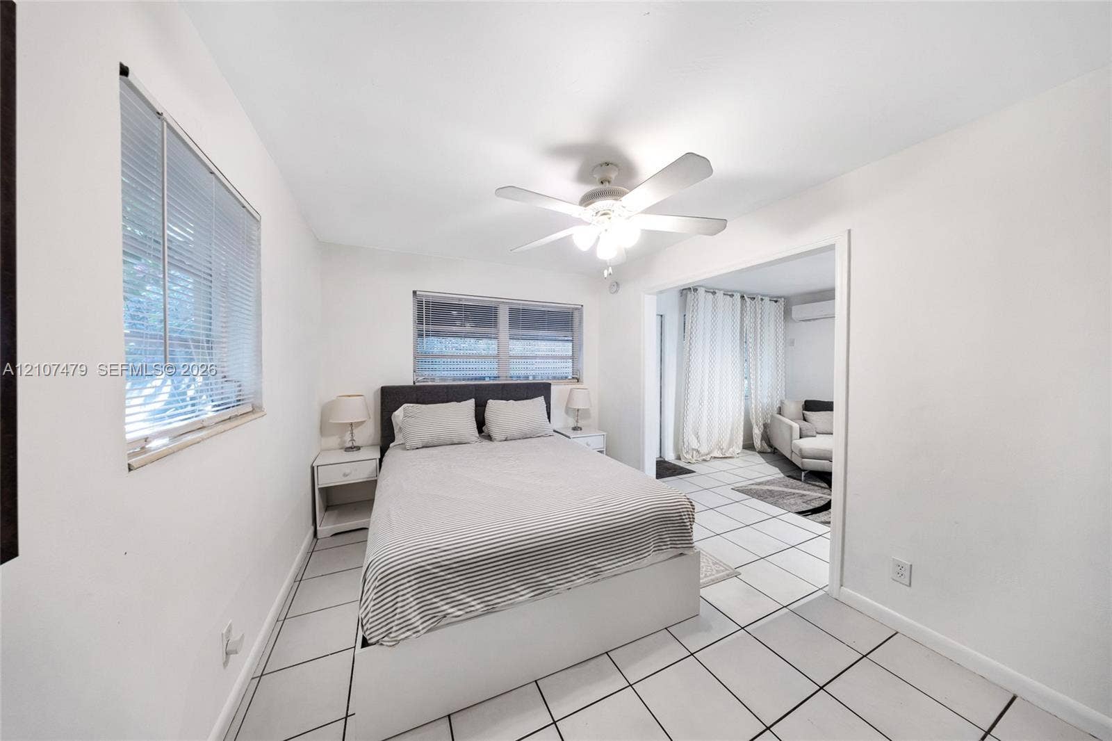 Interior space featuring large-format ceramic floor tiling, white walls, two windows with integrated blinds, and a central ceiling fan with integrated light fixture