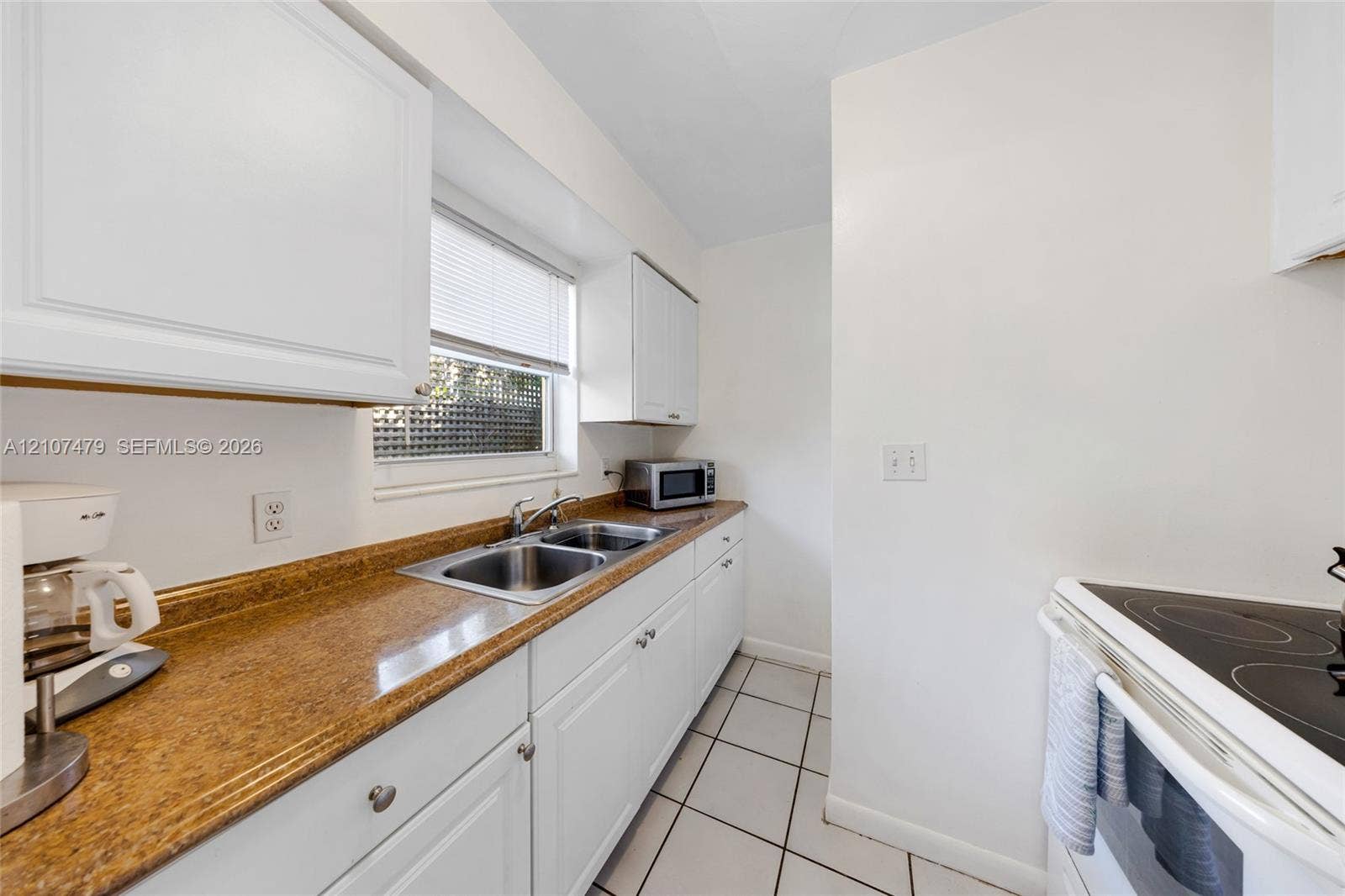 Kitchen featuring white shaker-style cabinetry, solid-surface countertops, dual-basin stainless steel sink, and ceramic tile flooring